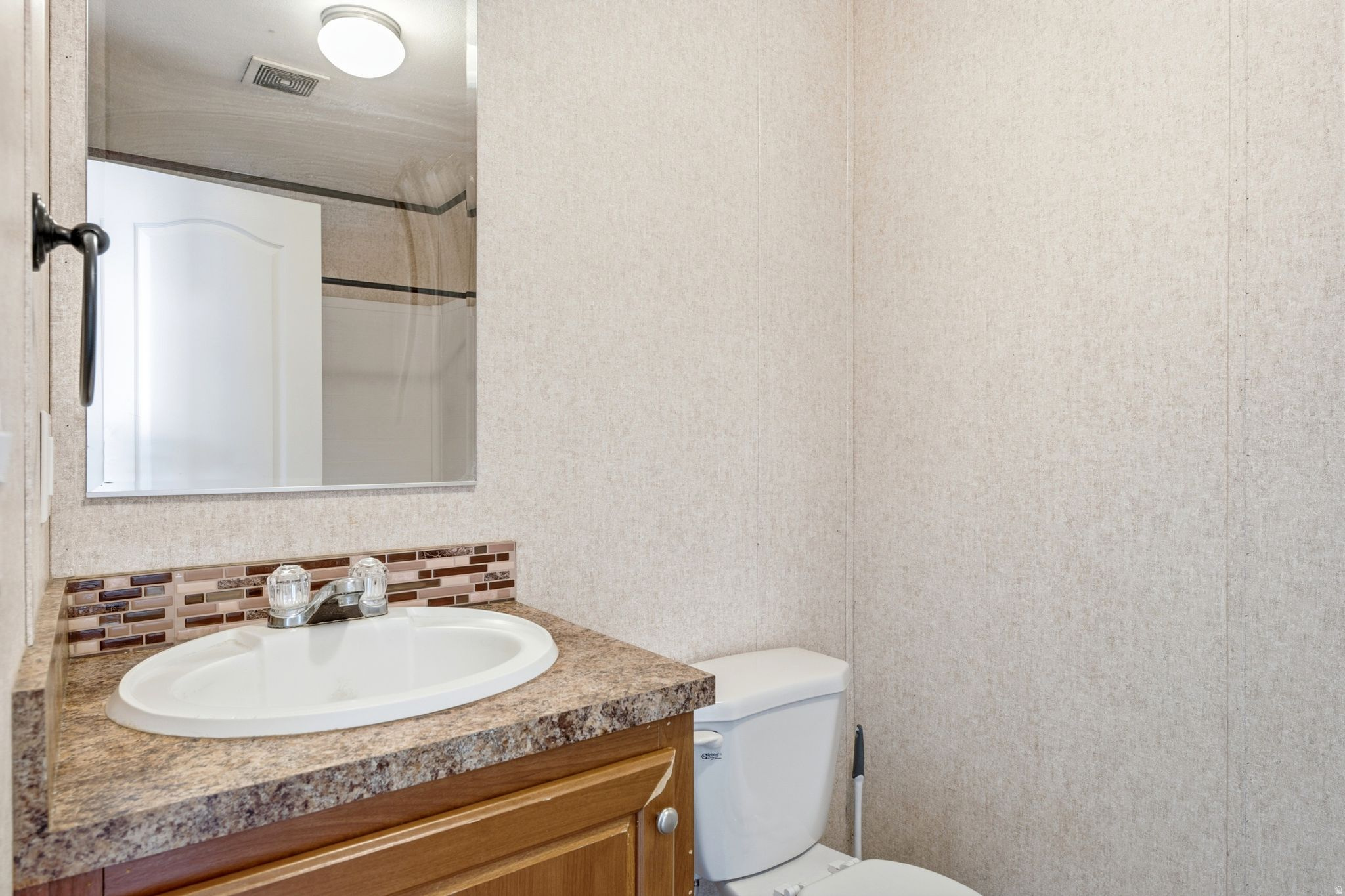 Bathroom vanity featuring a white oval sink, chrome faucet, and a brown patterned countertop with a mosaic tile backsplash