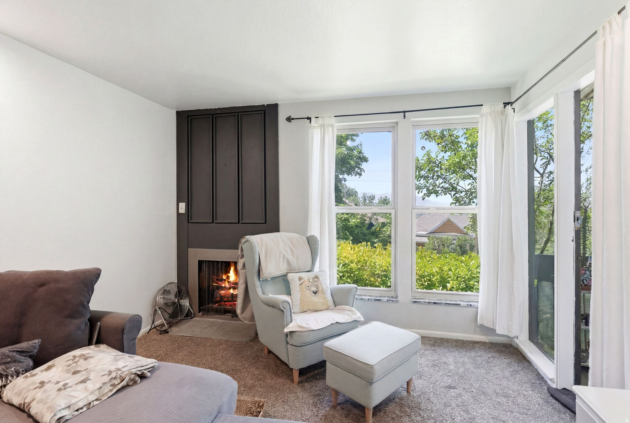 Living area with a dark paneled fireplace surround, multiple windows, and a glass door