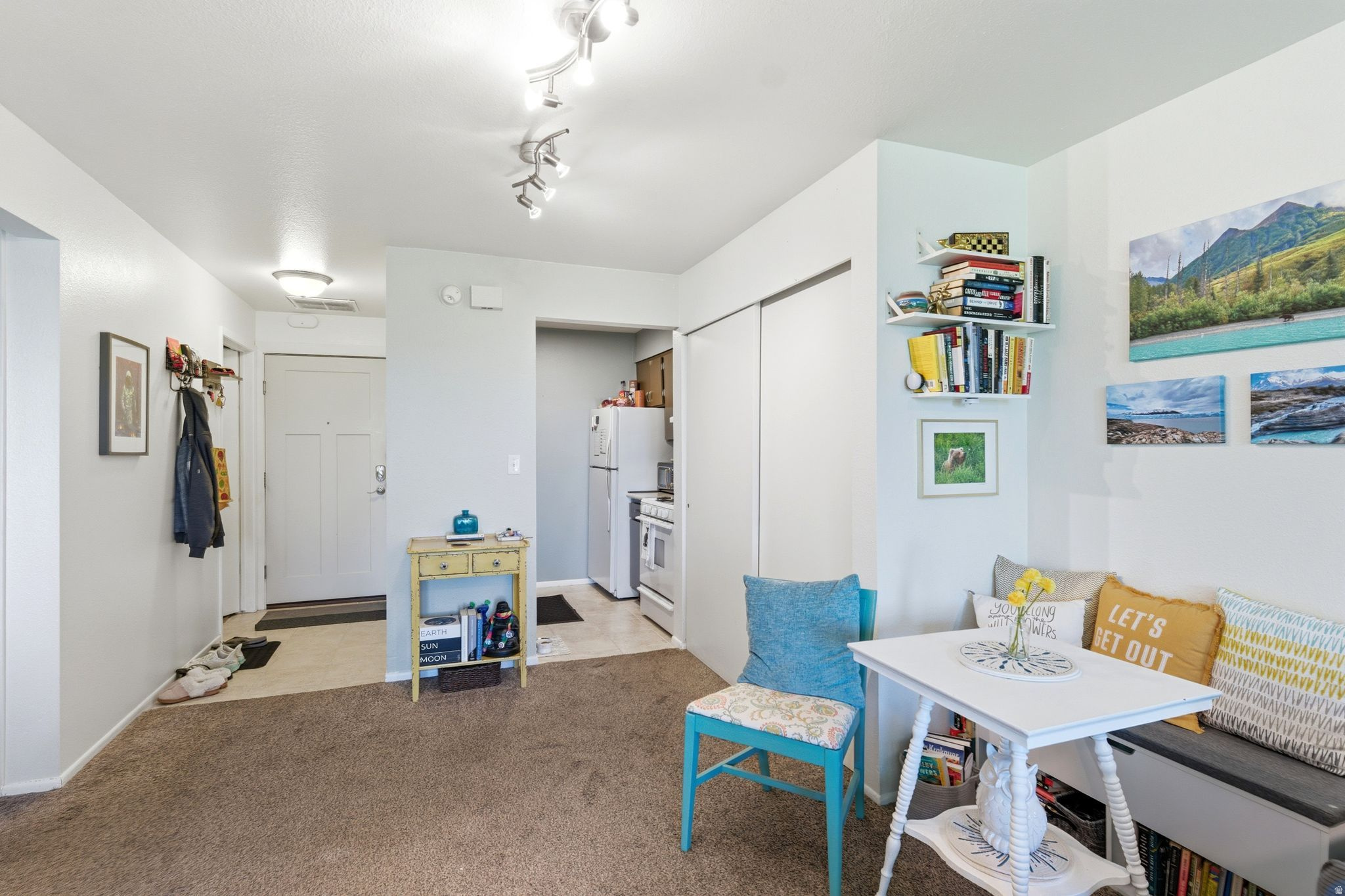 Interior living space featuring track lighting, a dedicated entry area with a paneled door, and a kitchen alcove with white appliances