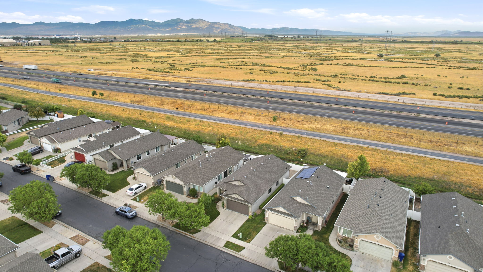 Aerial perspective showcasing a residential street with single-story homes, a multi-lane highway, and expansive arid terrain