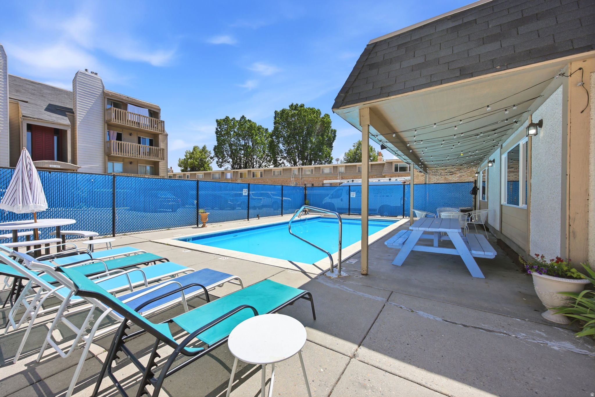 Outdoor swimming pool with concrete decking, surrounded by a blue privacy screen and chain-link fence