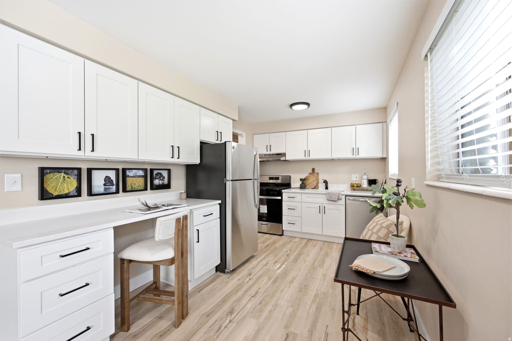 Modern kitchen featuring white shaker cabinetry with matte black hardware, light wood-finish flooring, stainless steel appliances, and solid surface countertops