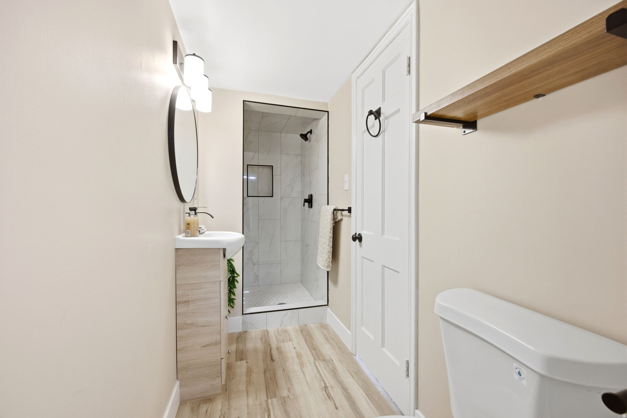 Bathroom featuring a walk-in shower with black frame, wood-finish flooring, and a pedestal sink with vanity