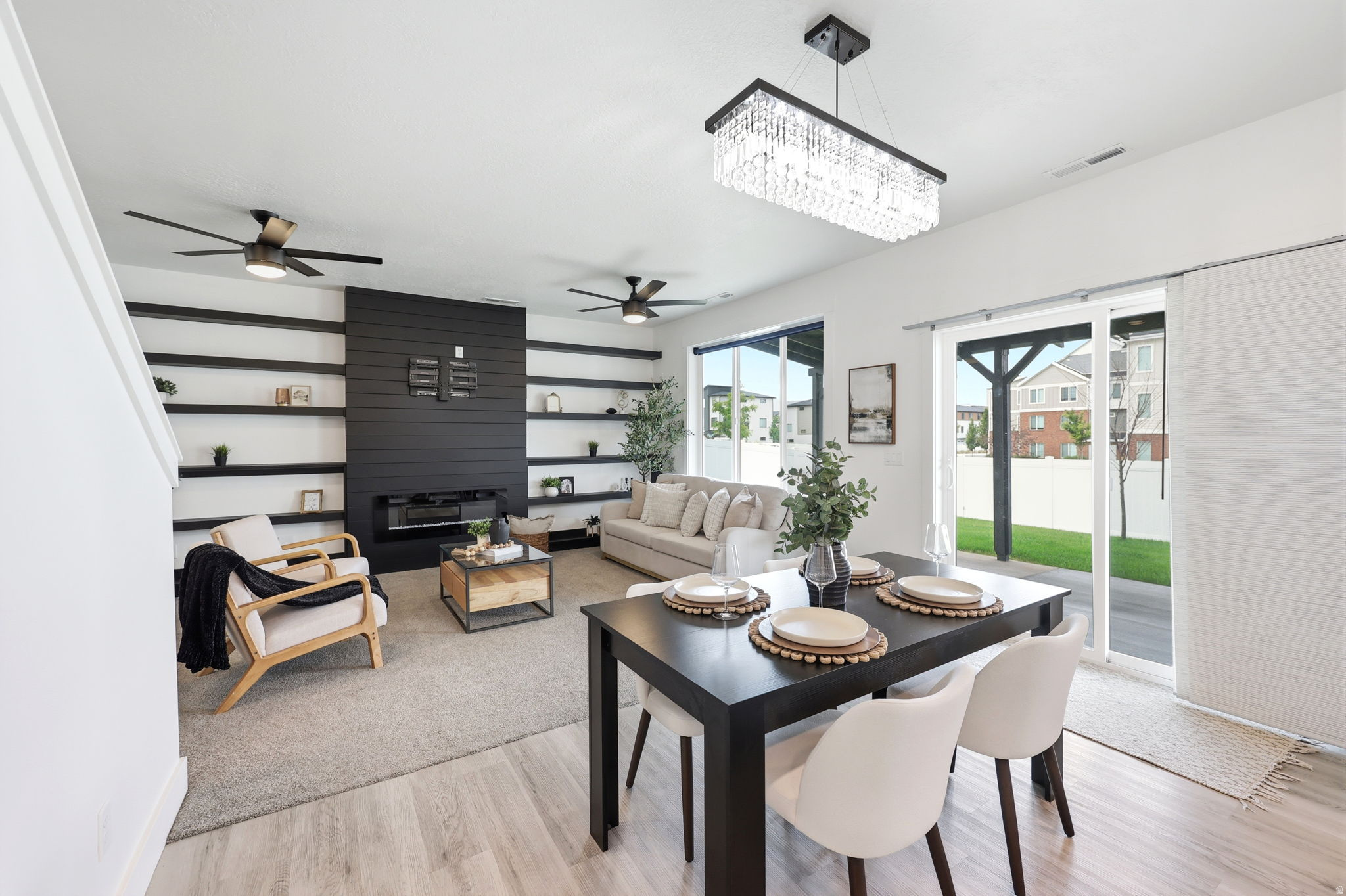 Open-concept living area with wood-finish flooring, a contemporary fireplace feature wall with built-in shelving, a modern rectangular chandelier, and a sliding glass door leading to the backyard
