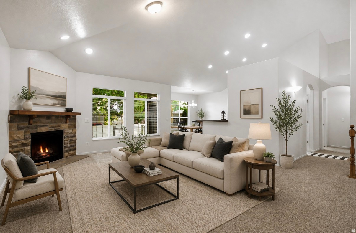 Bright and spacious living room featuring recessed ceiling lighting, a gas fireplace with stone surround, large multi-pane windows with natural light, neutral wood-finish flooring, and neutral upholstered seating areas anchored by a low-profile metal-fram