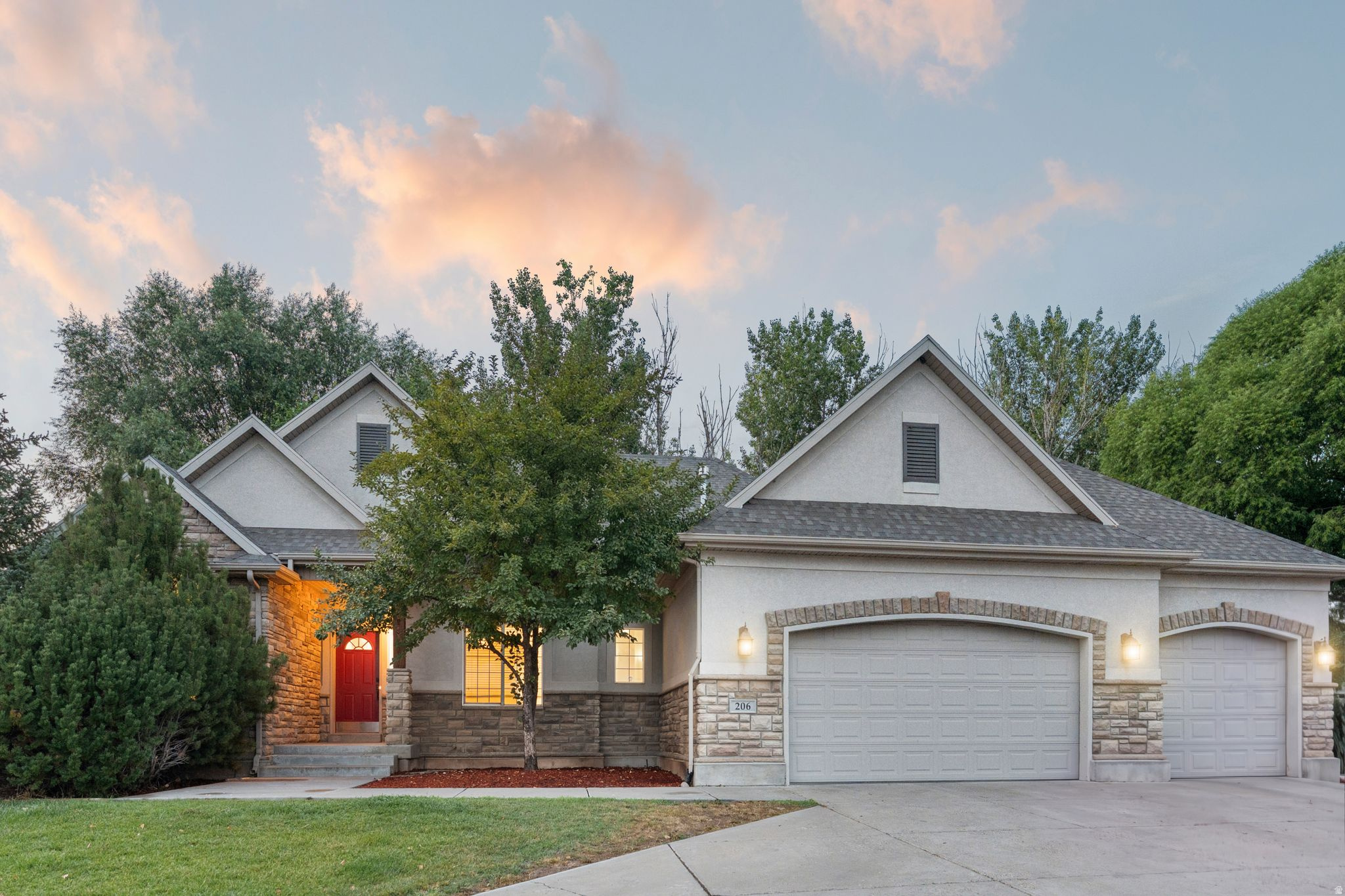 Exterior featuring a red entry door, stone and stucco facade, dual garage doors with arched brick accents, and a concrete driveway