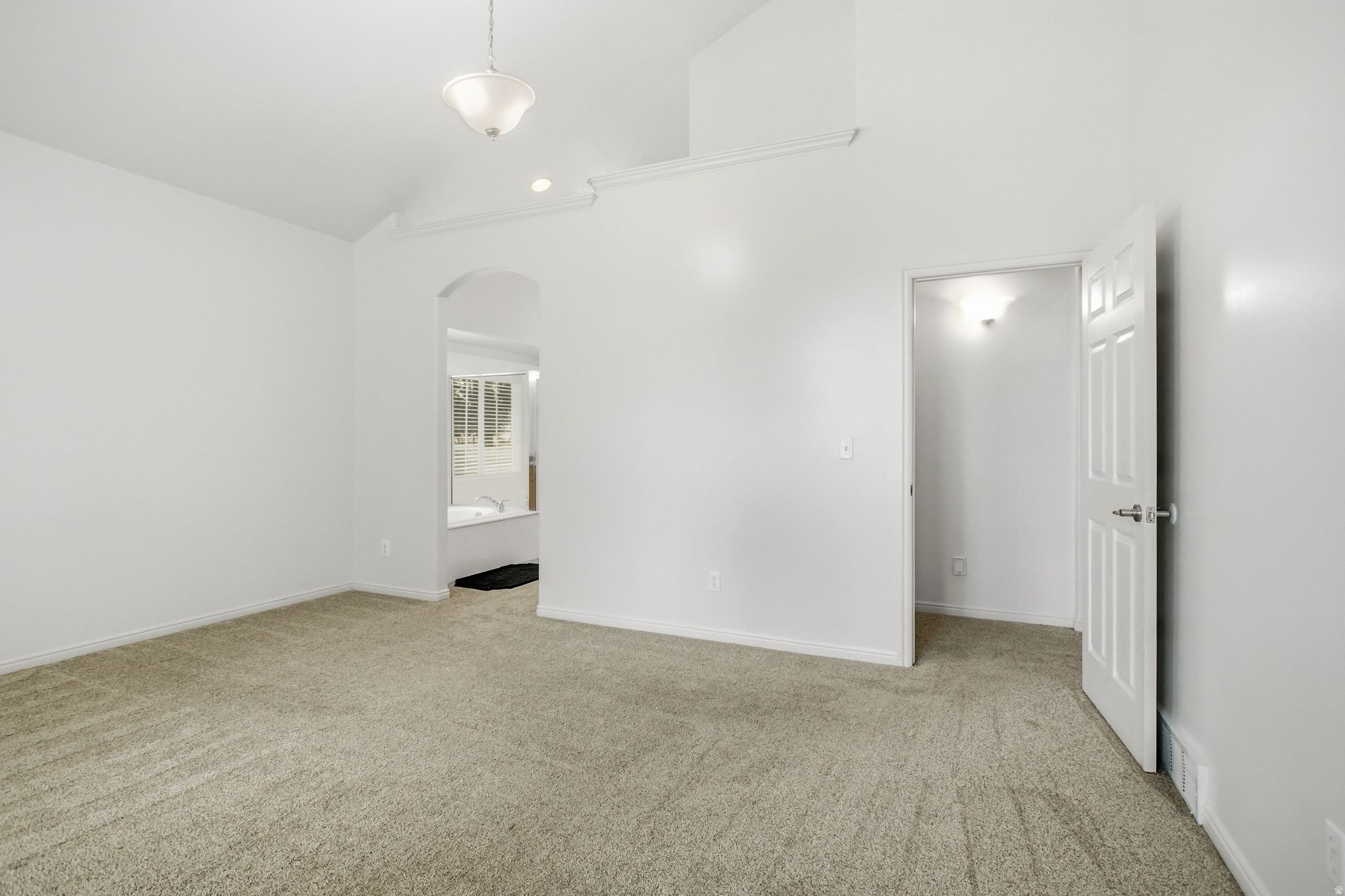 Carpeted room featuring a vaulted ceiling with a semi-flush mount light fixture and an arched doorway leading to a bath area with a built-in tub
