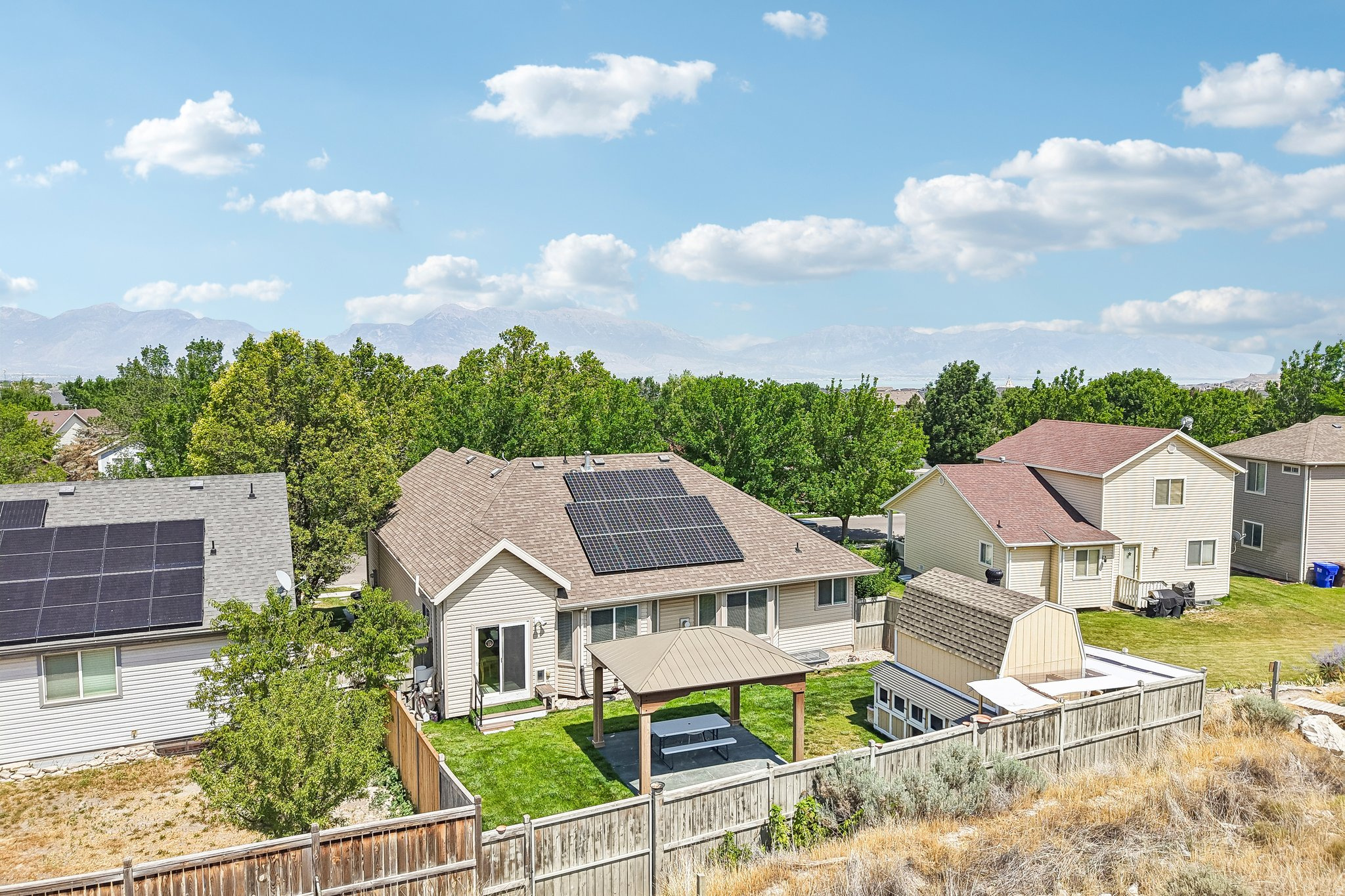 Rear exterior featuring a covered patio, fenced yard, solar panels, and mountain backdrop
