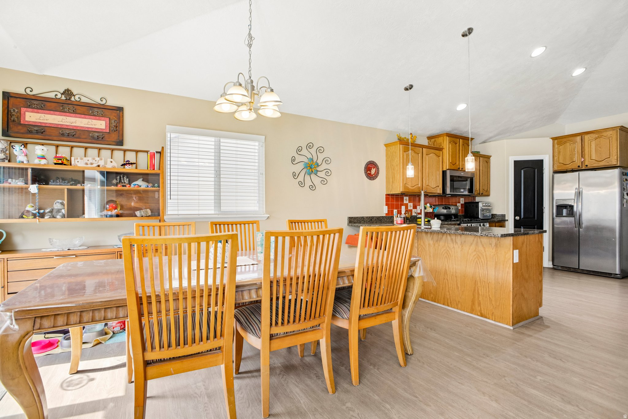 Open concept dining area and kitchen featuring vaulted ceilings, wood-finish flooring, wood cabinetry, and recessed lighting