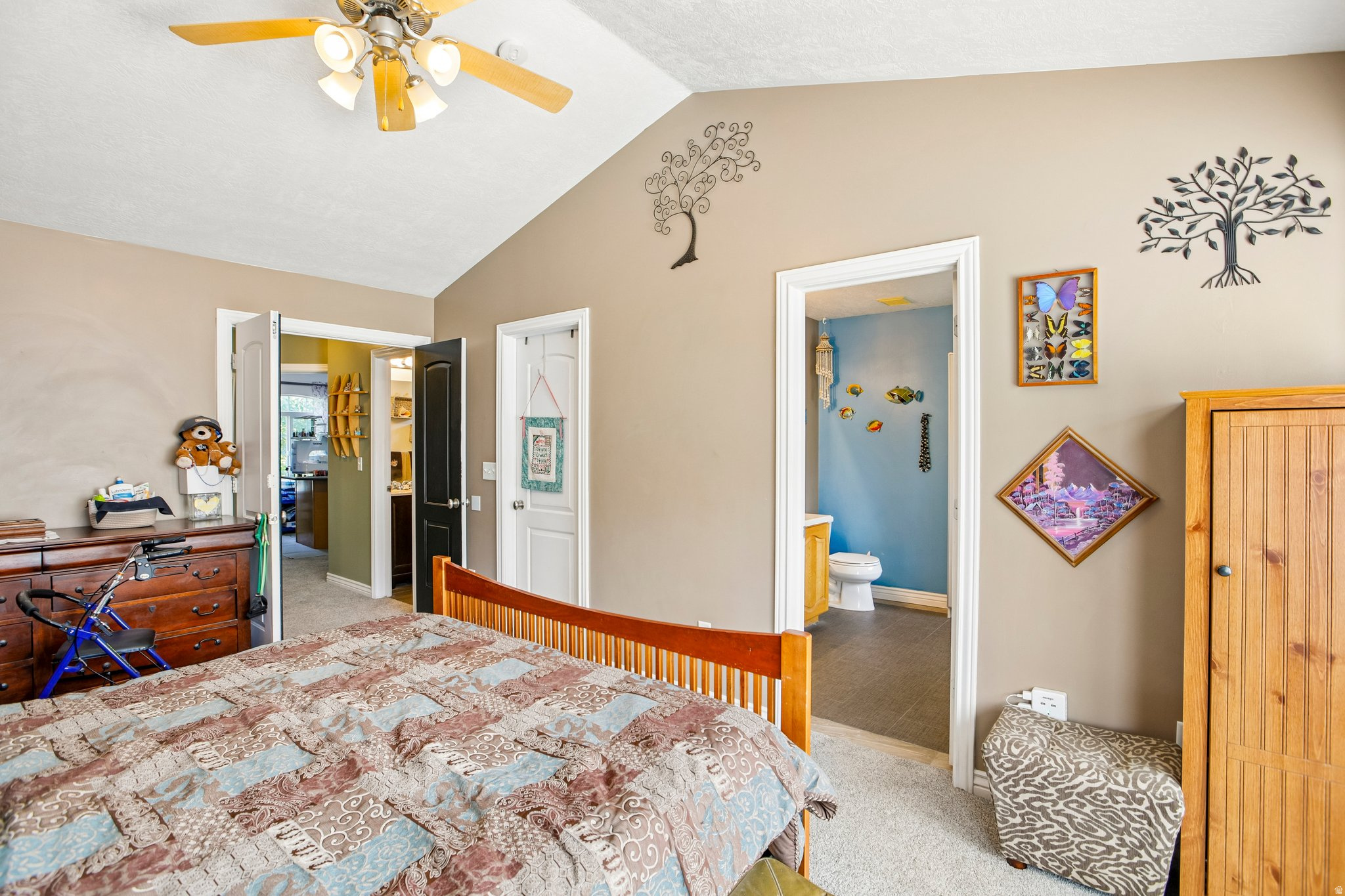Vaulted ceiling bedroom featuring a ceiling fan with integrated lighting, carpet flooring, and an en-suite bathroom with a built-in vanity and toilet