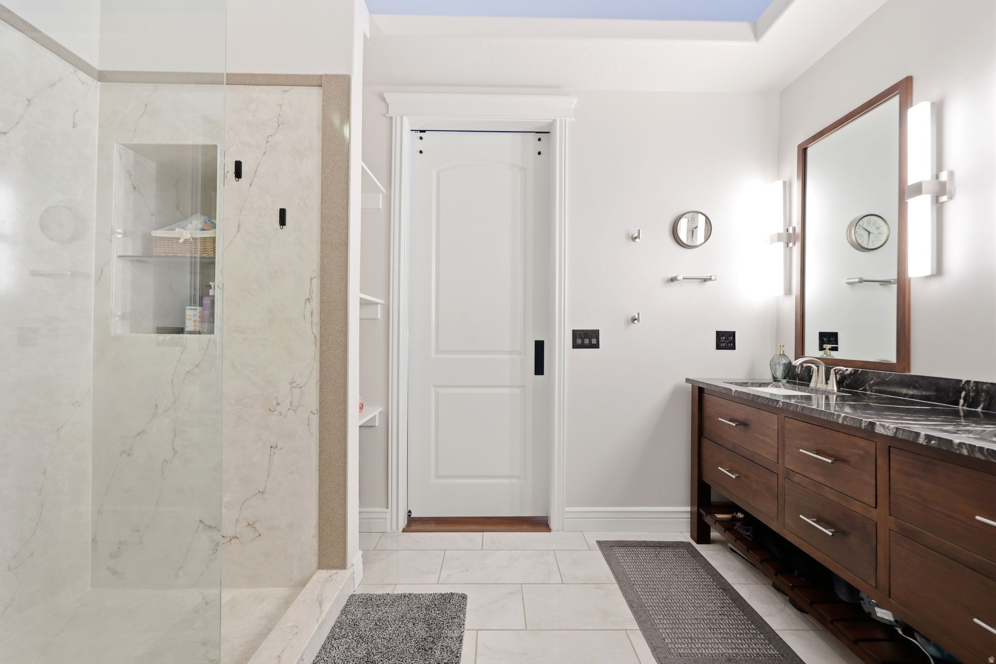 Bathroom featuring a spacious walk-in shower with light-toned stone-look tile, a built-in shower niche, and a glass enclosure