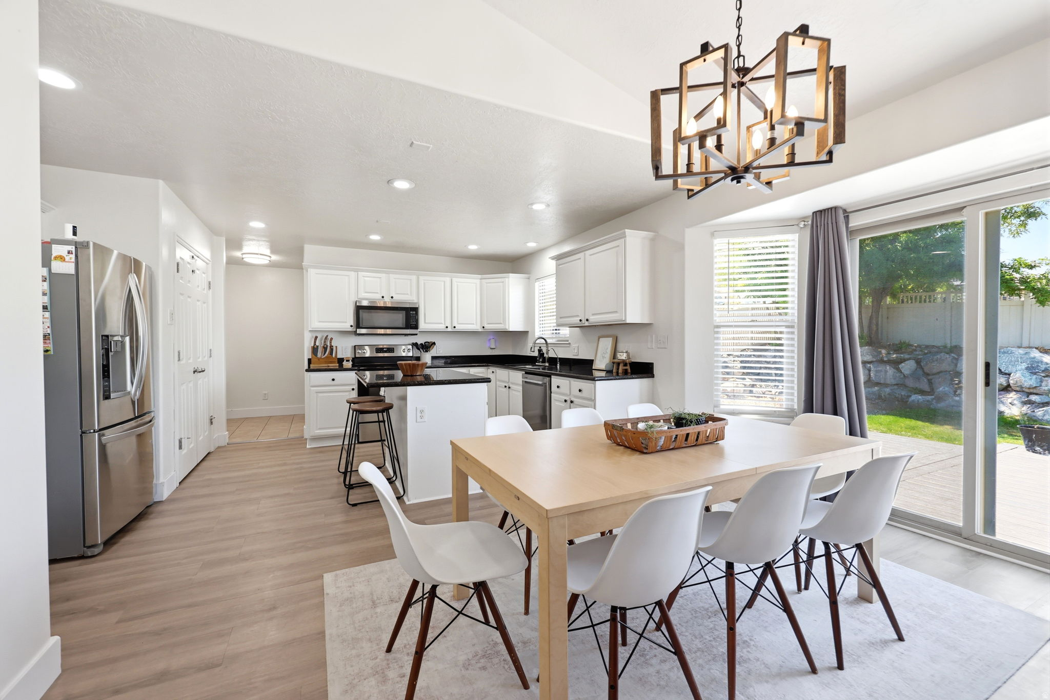 Open concept kitchen and dining area featuring light wood-finish flooring, white cabinetry, dark countertops, and stainless steel appliances