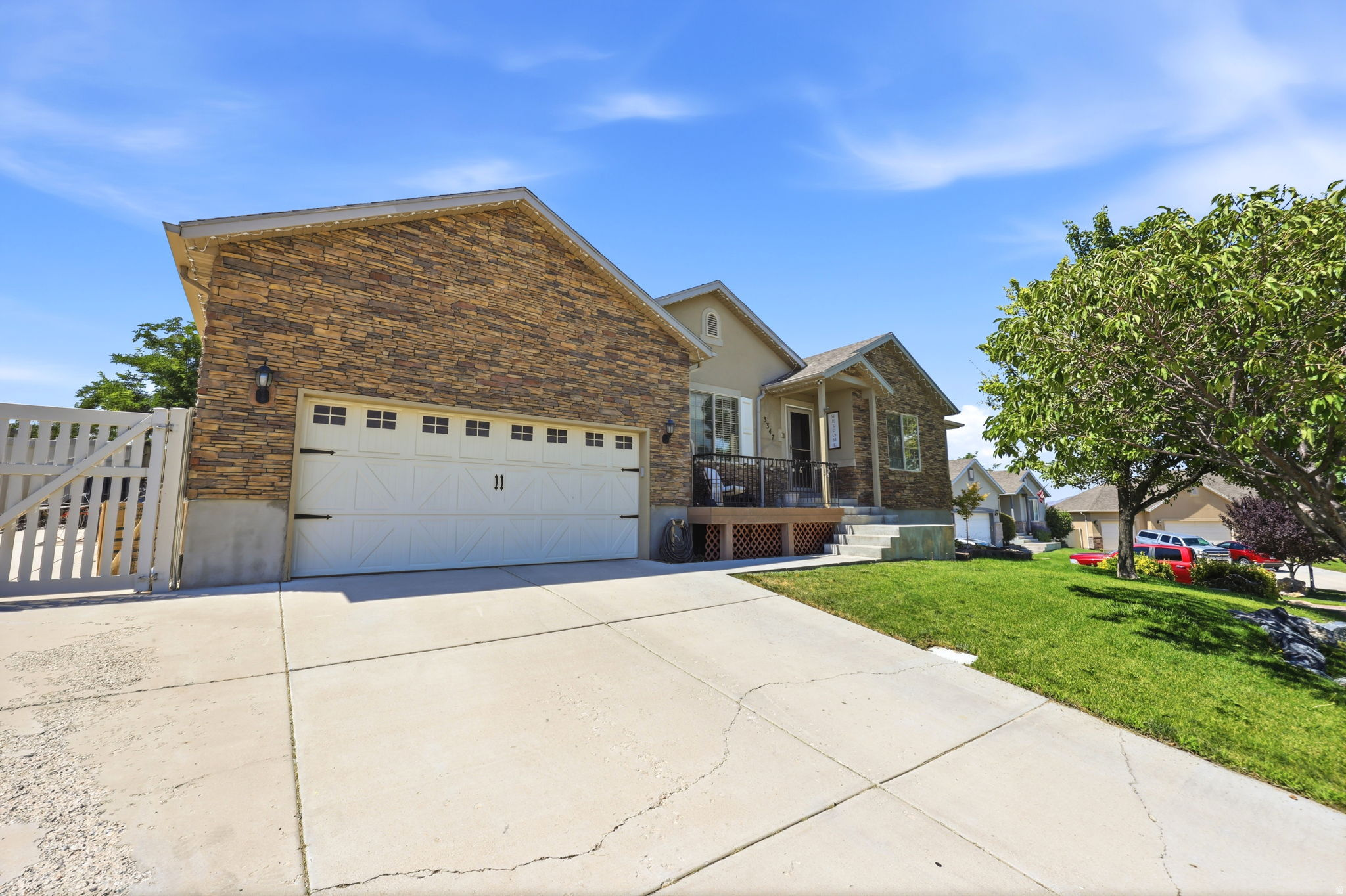 Exterior featuring a stone facade, beige siding, white garage door with decorative hardware, a covered porch, and a concrete driveway
