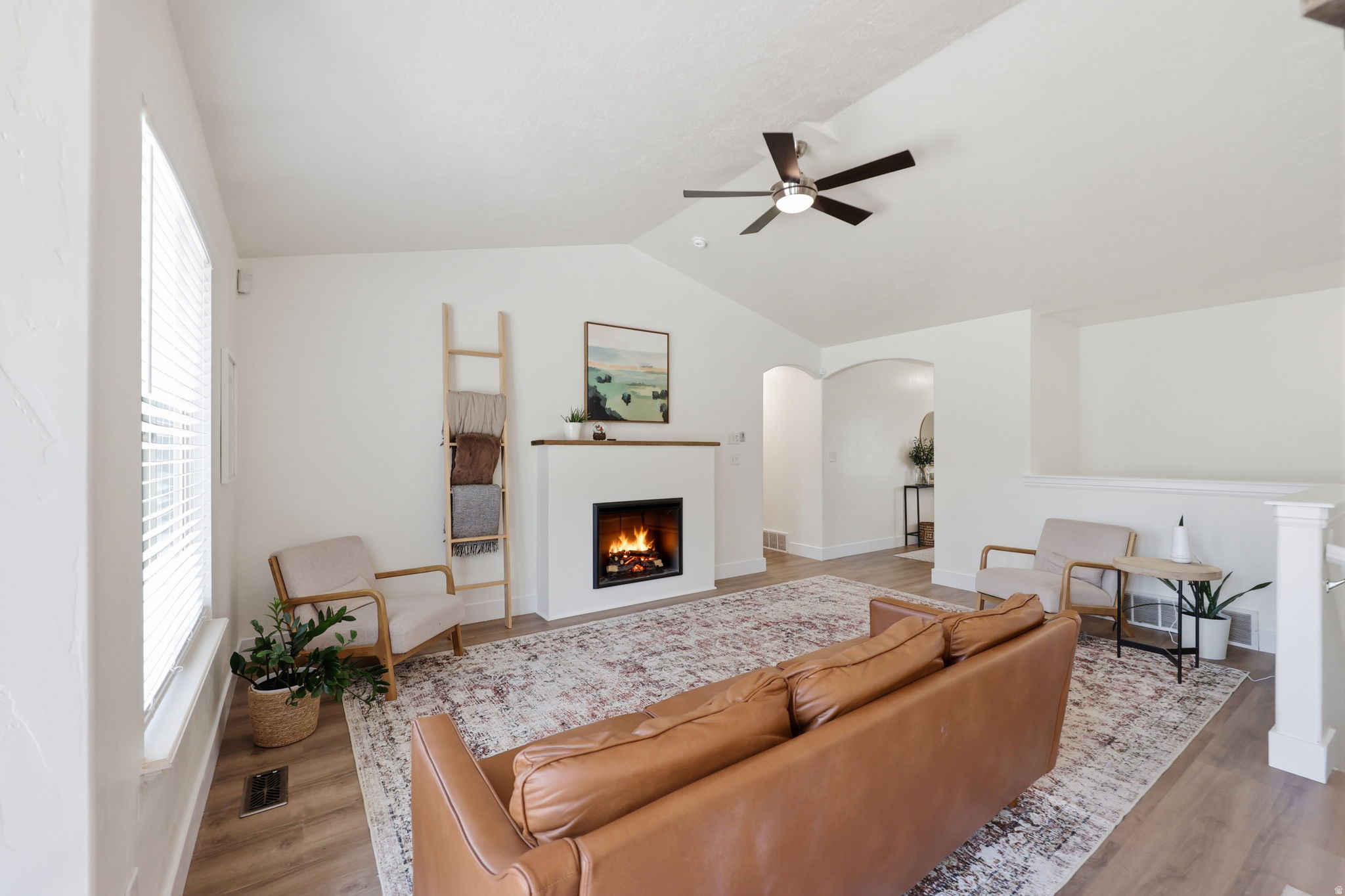 Living area featuring a fireplace with a wood mantle, vaulted ceilings, and a ceiling fan