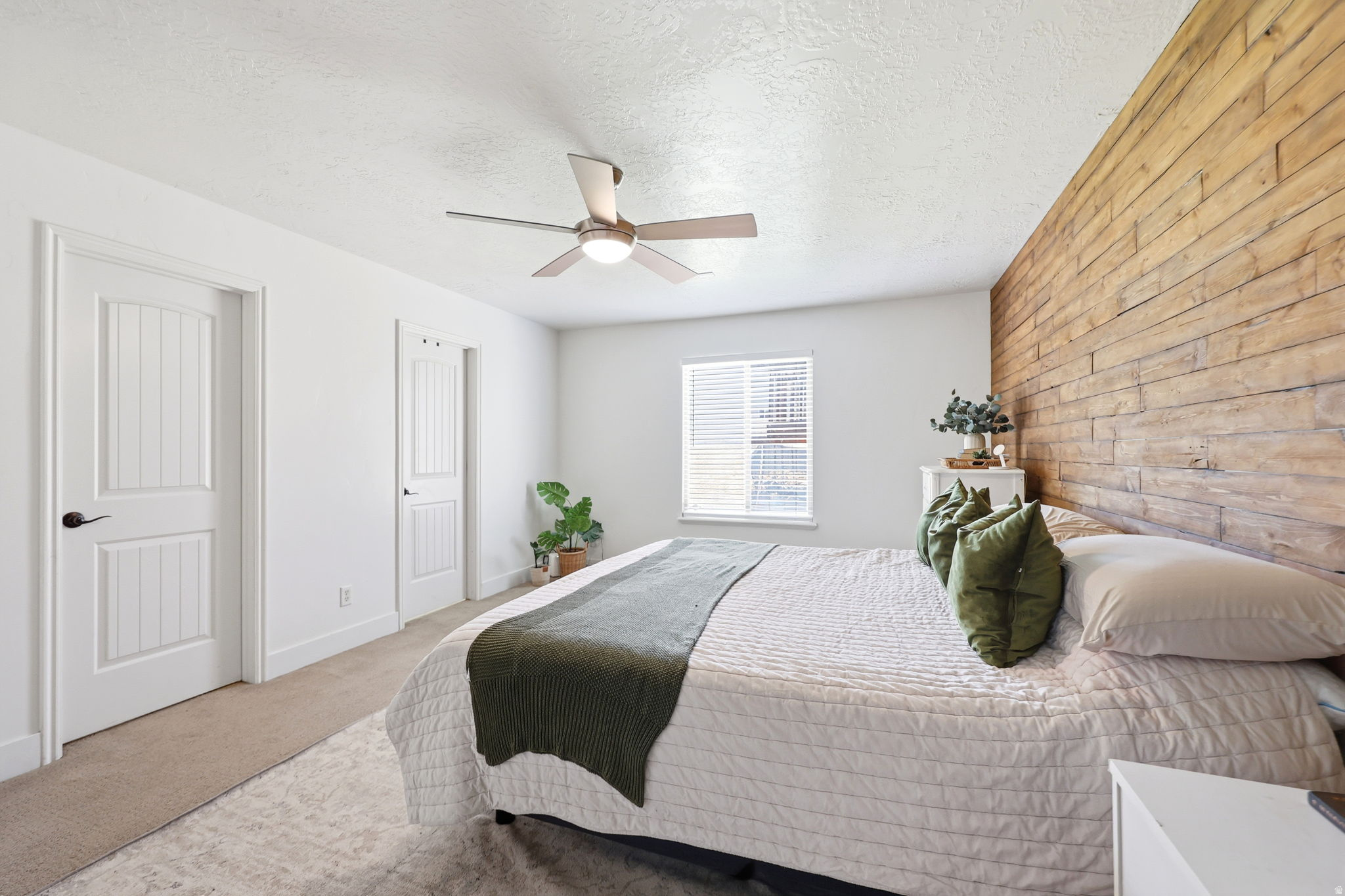Bedroom featuring a plank wood accent wall, neutral carpeting, and a ceiling fan with integrated lighting