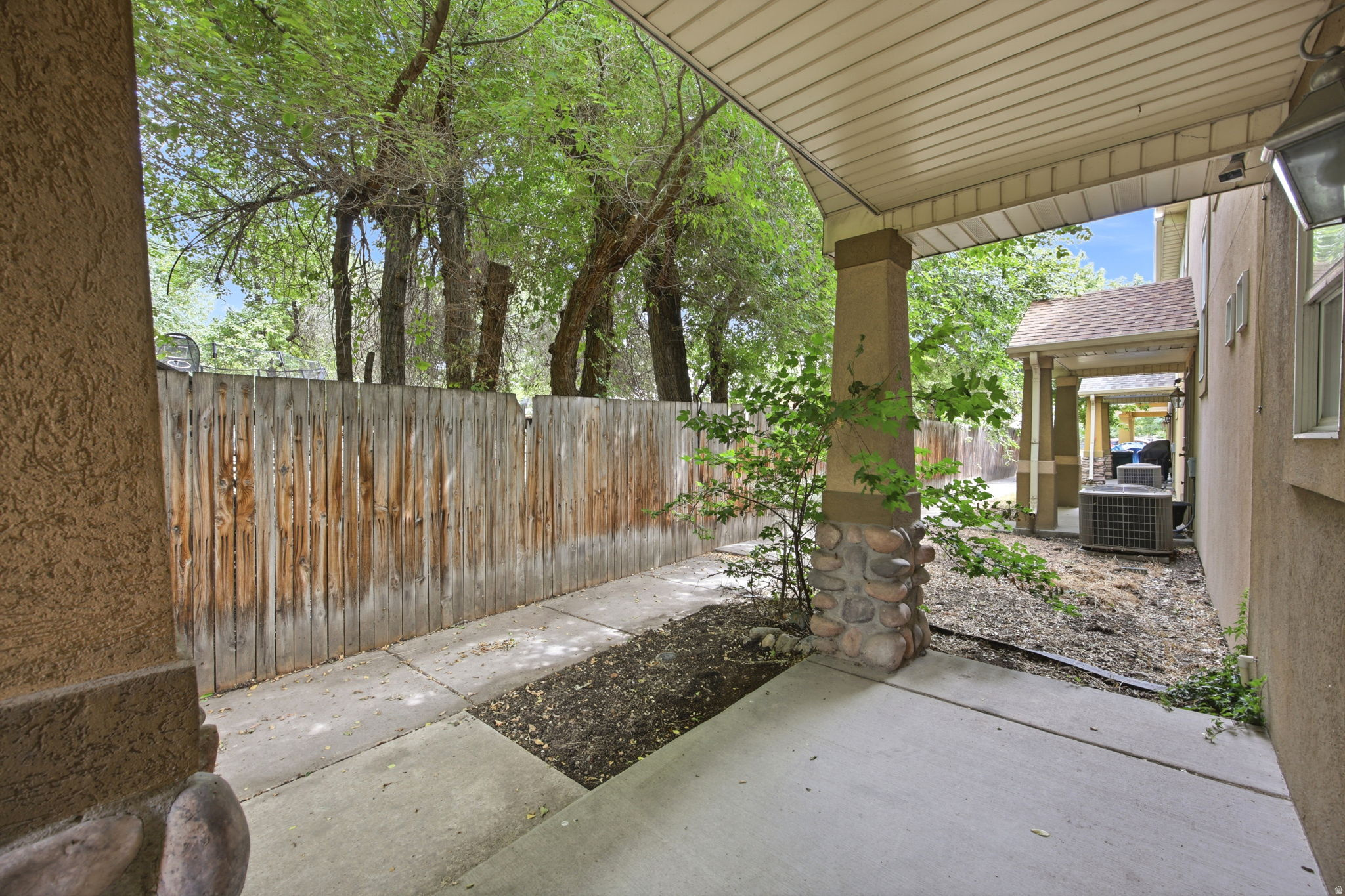 Covered patio area with concrete flooring, stone-clad pillar, and textured stucco wall