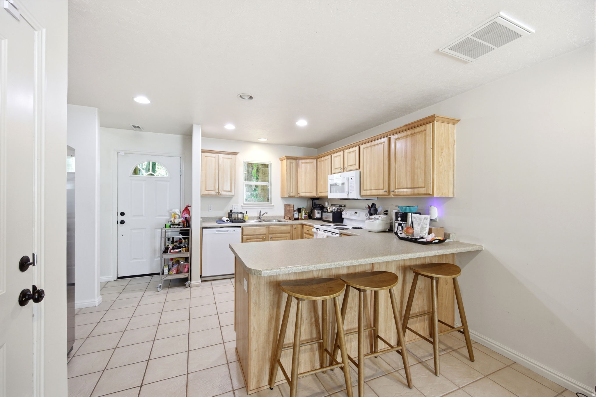 Spacious kitchen featuring light wood-finish cabinetry, a large peninsula with a countertop extension, recessed lighting, and tile flooring