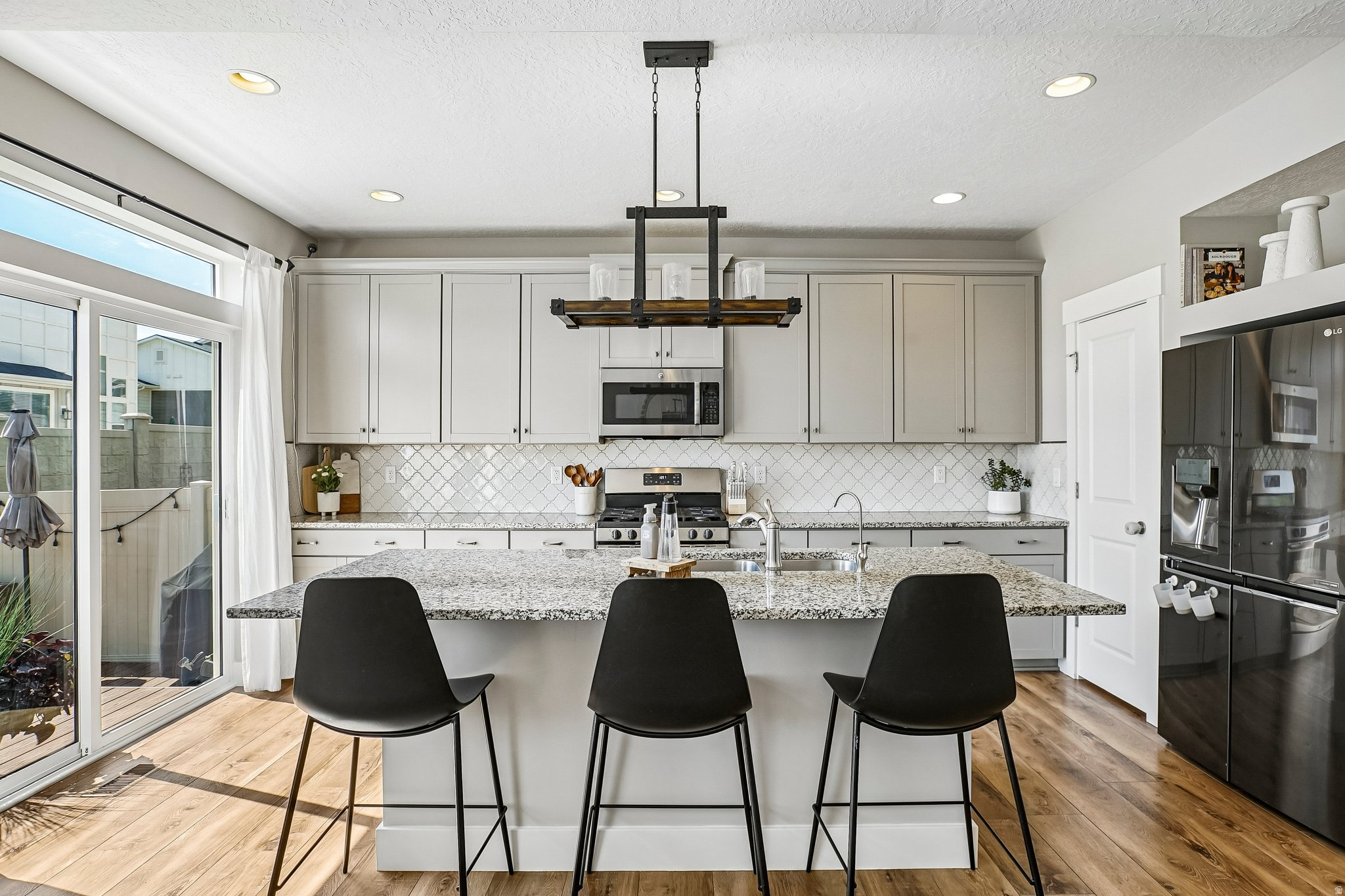 Modern kitchen featuring a central island with a speckled countertop, stainless steel appliances, white cabinetry, and wood-finish flooring