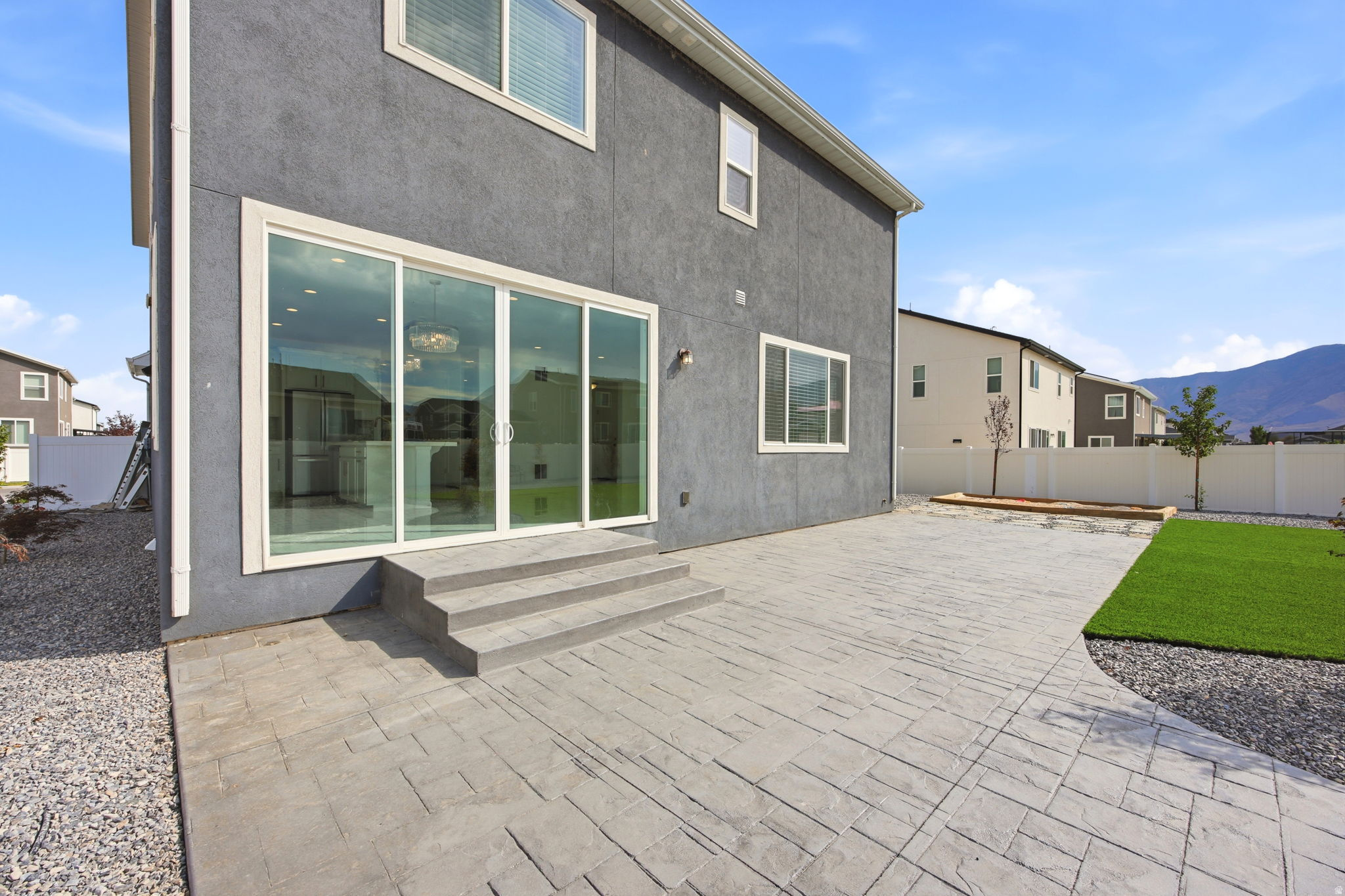 Rear exterior featuring a textured gray facade, multi-panel sliding glass door, and a patterned concrete patio with steps