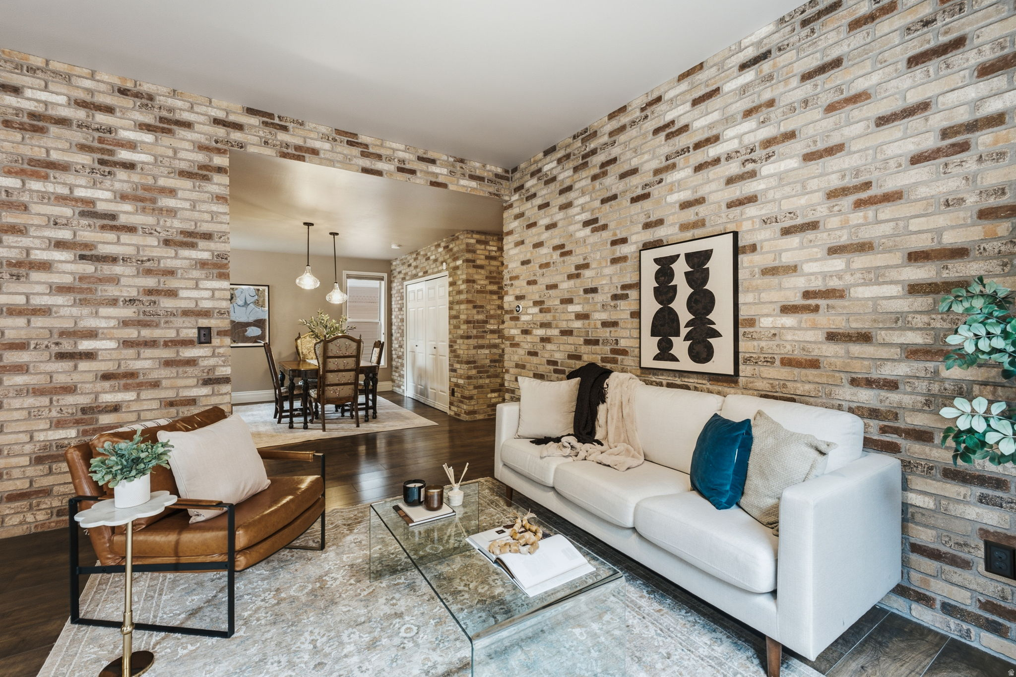 Interior living space featuring exposed brick walls, dark wood-finish flooring, and an open architectural feature to a dining area