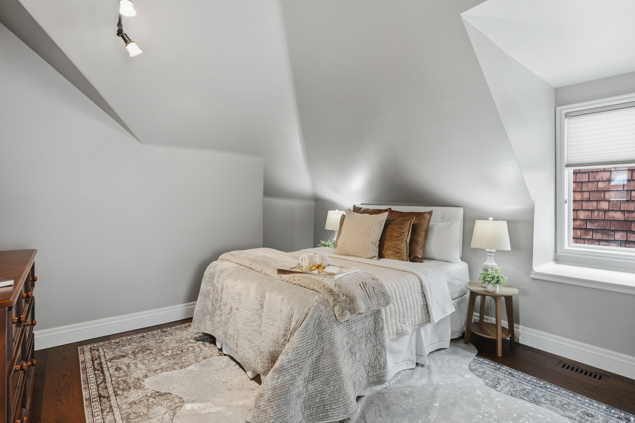 Attic bedroom featuring dark wood-finish flooring, light grey walls, and a prominent window with white trim