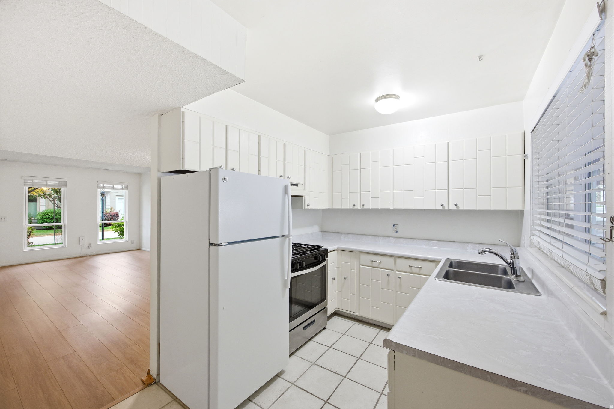 Well-equipped kitchen featuring white cabinetry, a double-basin stainless steel sink, and white tile flooring
