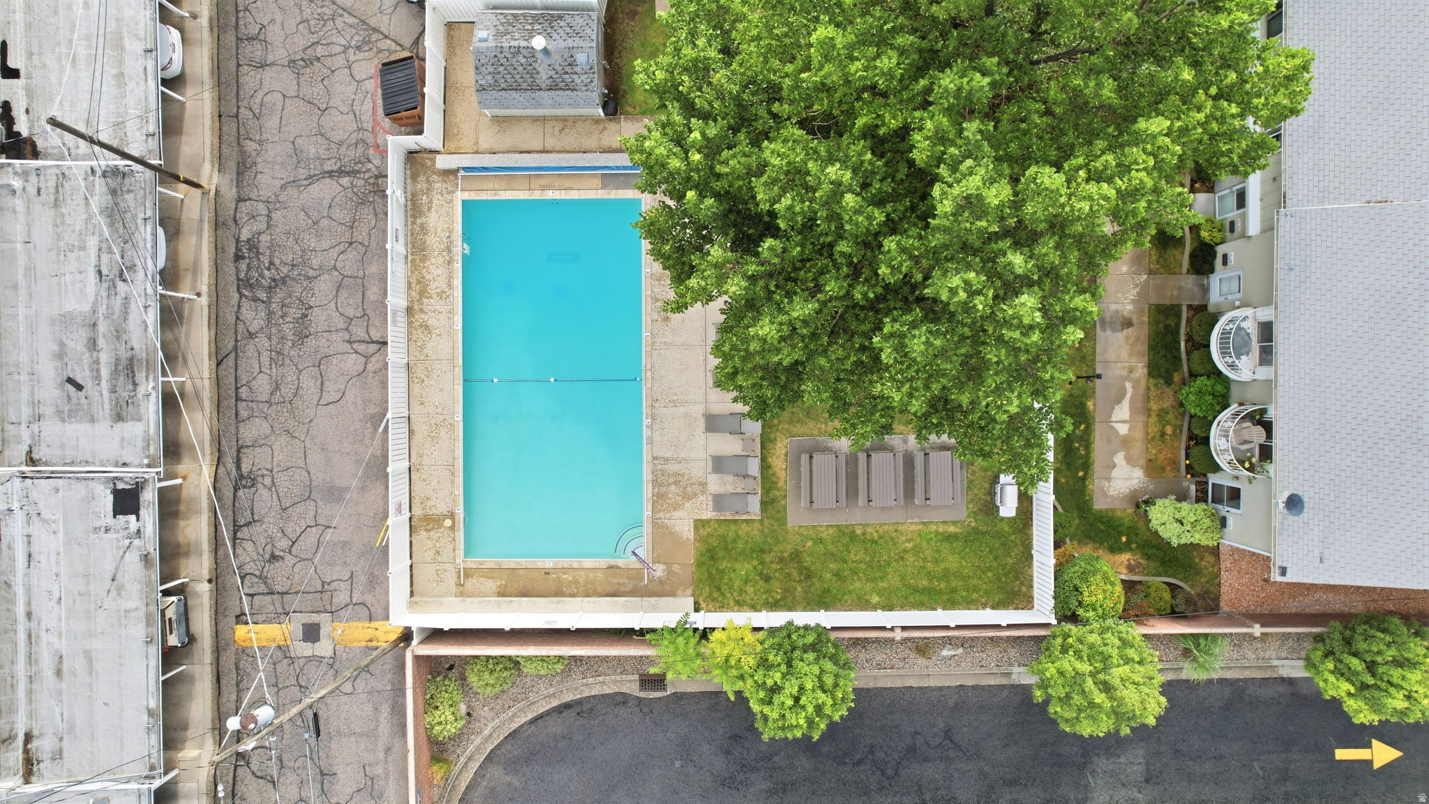 Rectangular swimming pool surrounded by a concrete patio and white fencing. Clubhouse connected to pool.