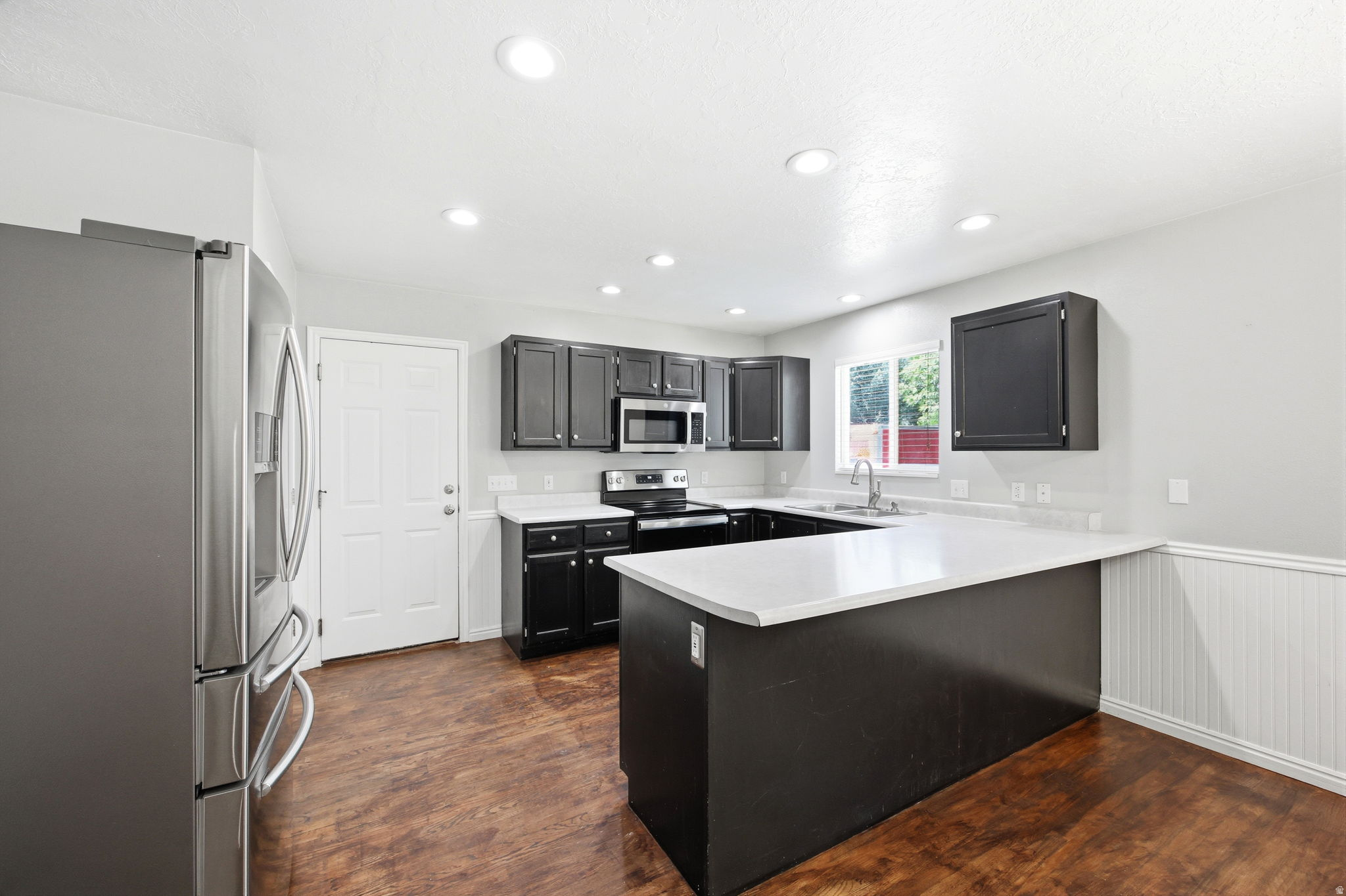 Kitchen featuring dark wood-finish cabinetry, light countertops, wood-finish flooring, recessed lighting, and stainless-steel appliances