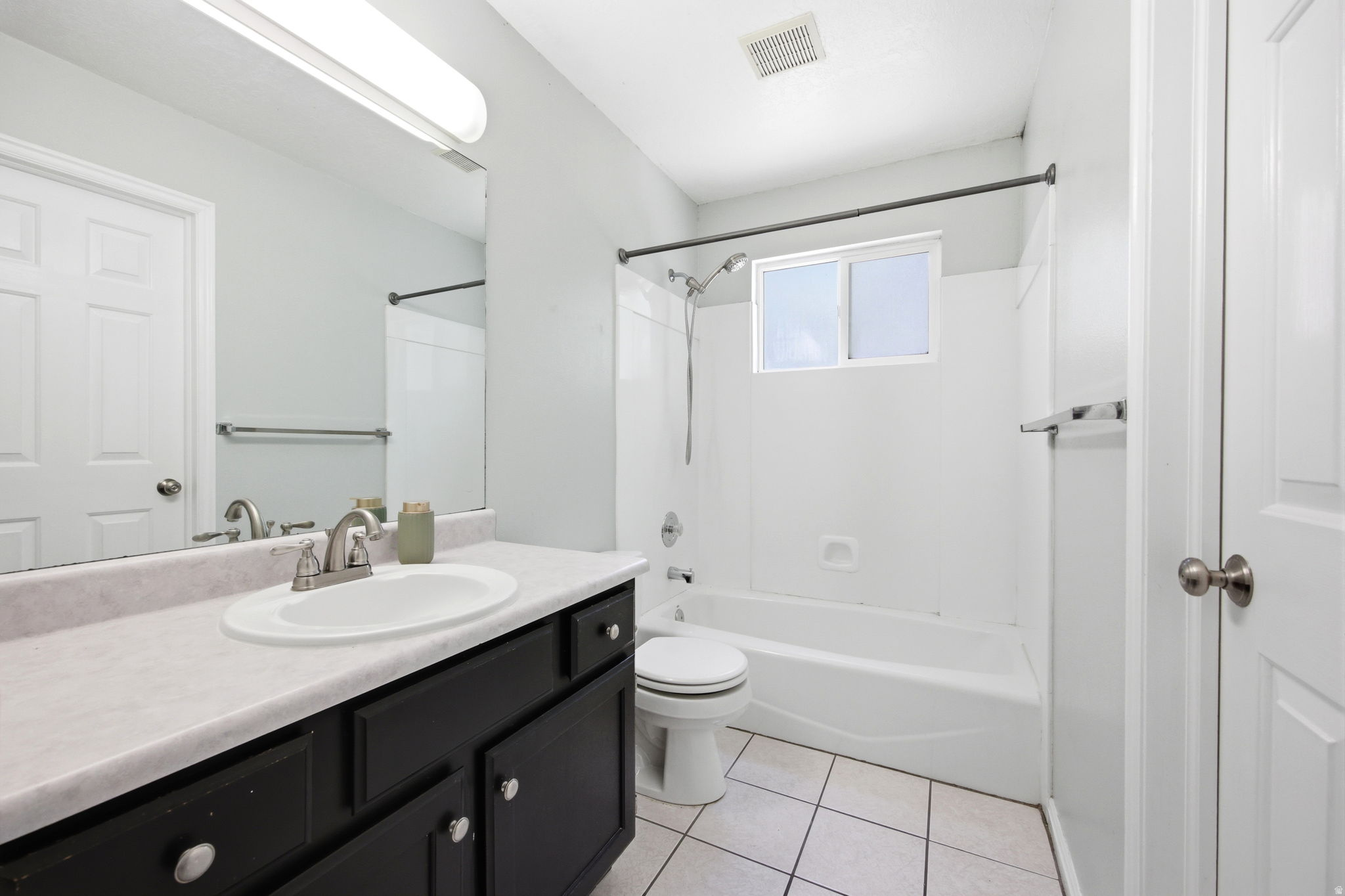 Full bathroom featuring a dark vanity with a light-colored countertop, an integrated sink with brushed nickel fixtures, a tub-shower combination with a window, and white tile flooring