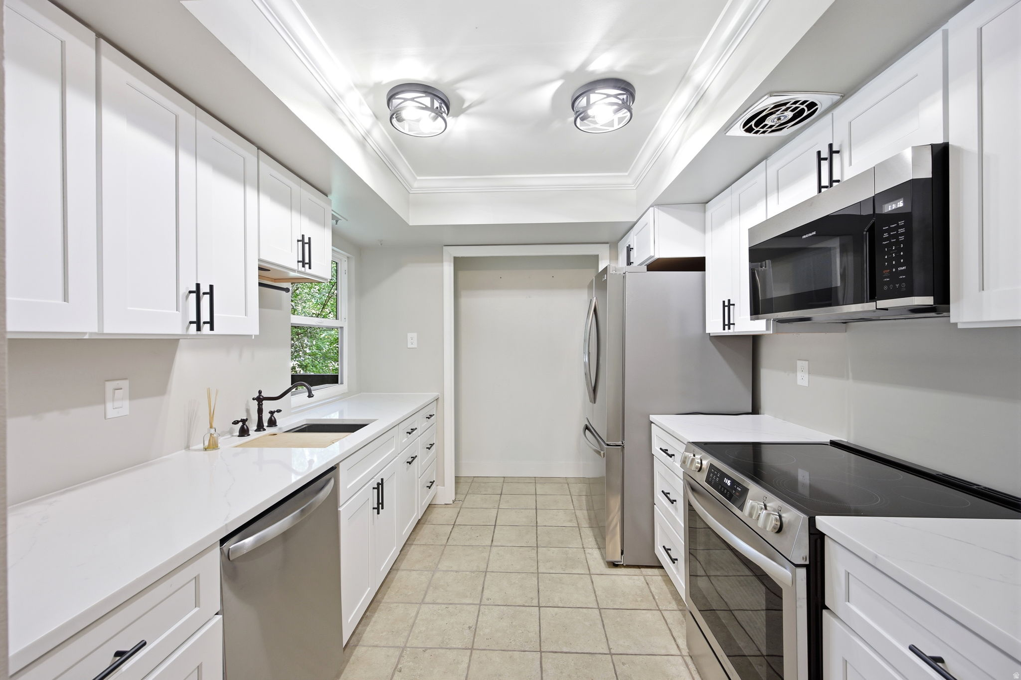 Galley kitchen featuring white cabinetry, stainless steel appliances, white countertops, and tile flooring.