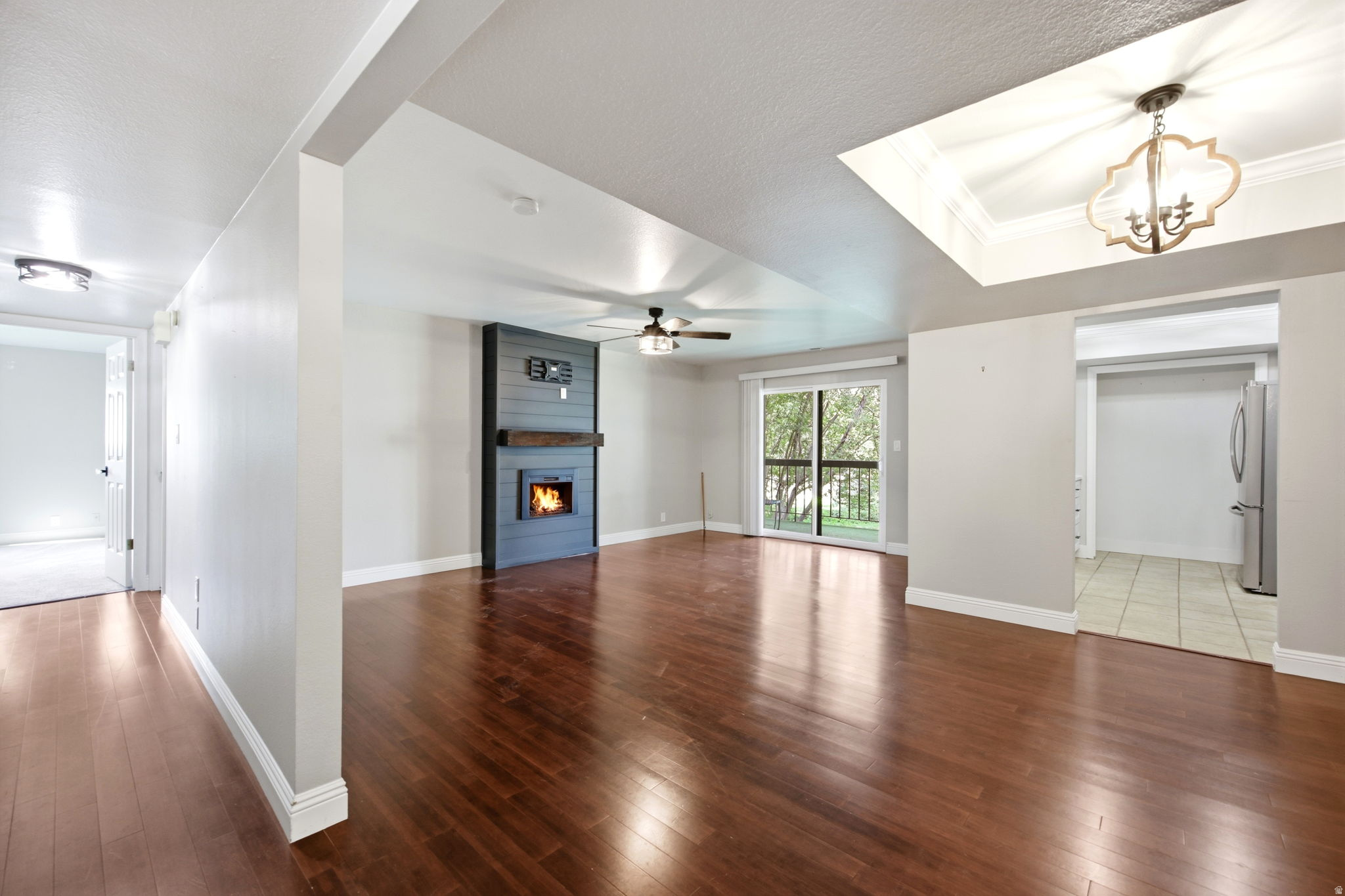 Spacious living area featuring rich wood-finish flooring, a contemporary fireplace with mantel, a ceiling fan, and sliding glass doors opening to outdoor space