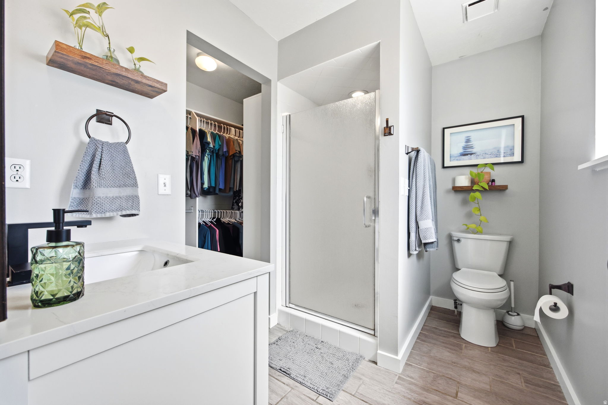 Bathroom featuring a walk-in shower with a frosted glass door, a white vanity with a light-toned countertop and integrated sink, and wood-finish flooring
