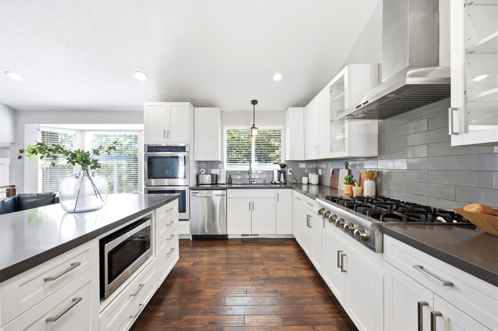 Modern kitchen featuring white cabinetry, dark countertops, wood-finish flooring, a built-in microwave drawer, and stainless steel appliances including a gas range and double wall ovens
