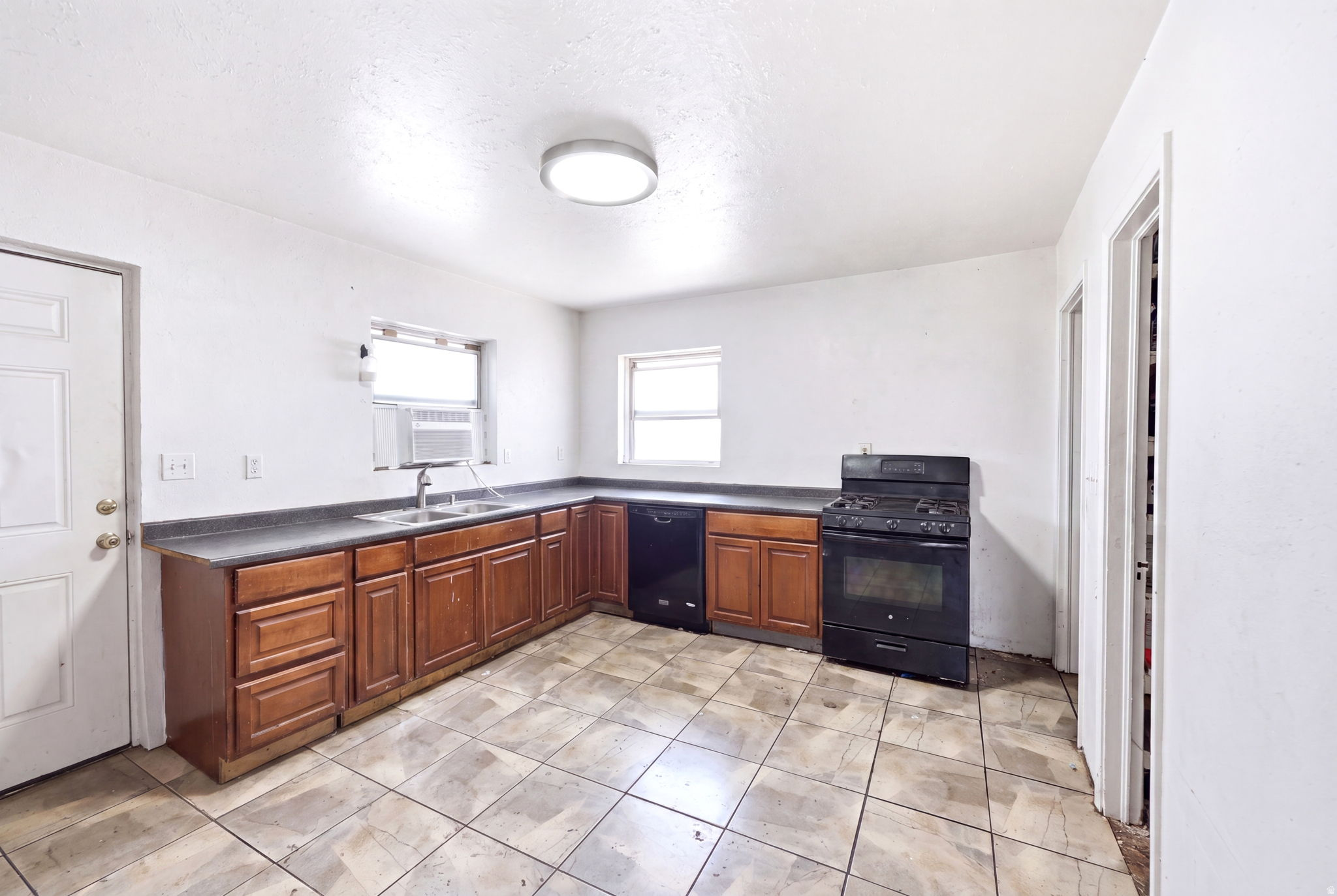 Kitchen featuring a L-shaped counter, wood-finish cabinetry, black appliances including a range and dishwasher, and tile flooring