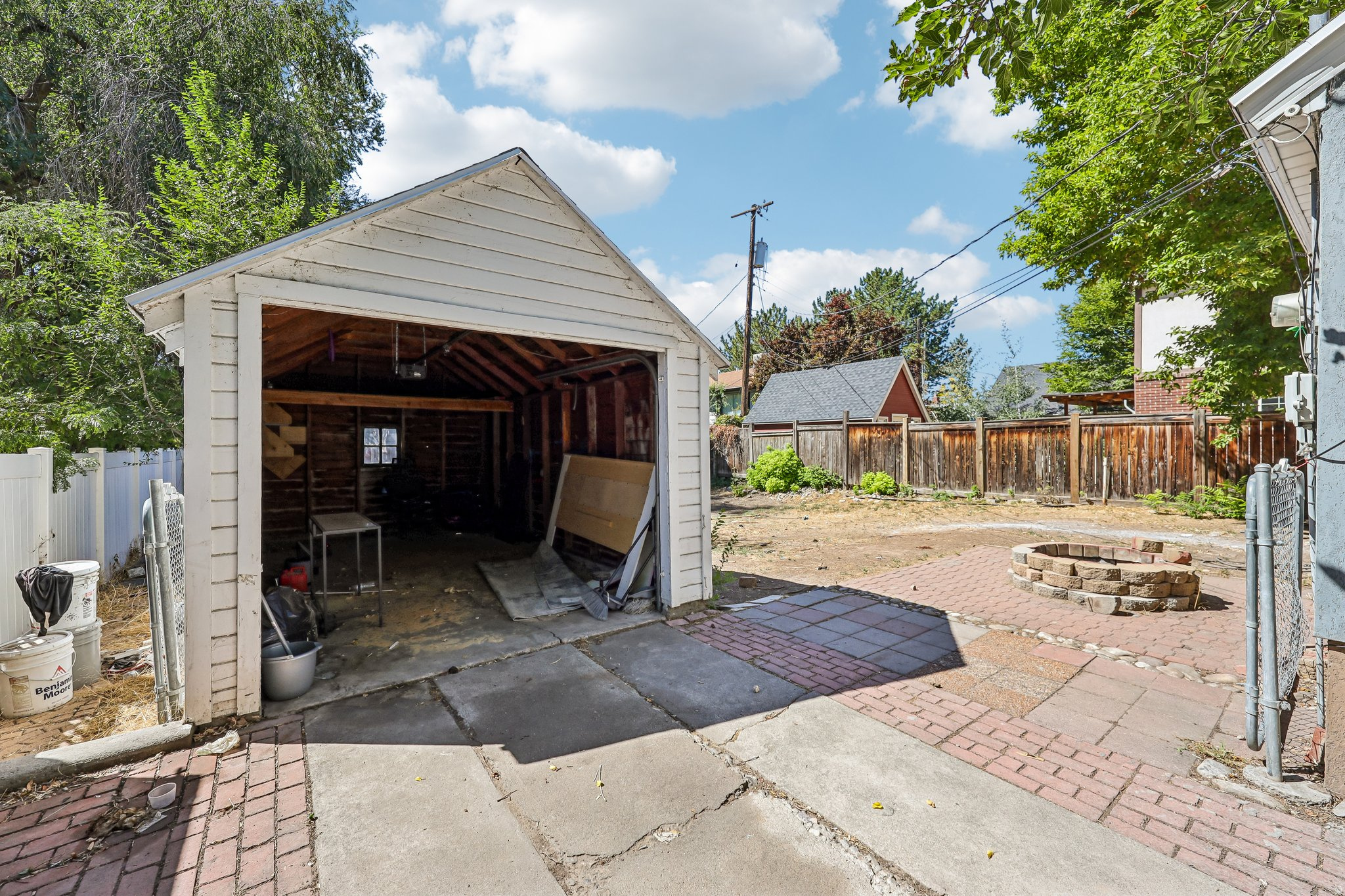 Detached garage with wood siding, concrete driveway, brick paver patio, stone fire pit, and wood fencing