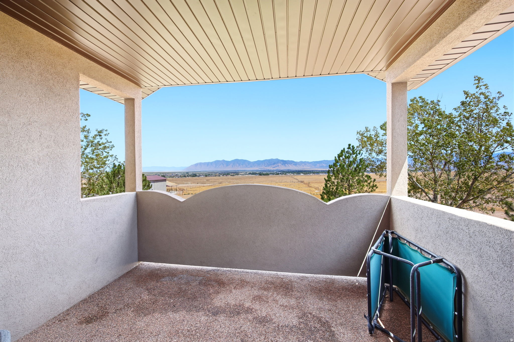 Main home - Master bedroom covered balcony with a textured floor and stucco walls, featuring a slat ceiling and open-air views of distant mountains and surrounding vegetation