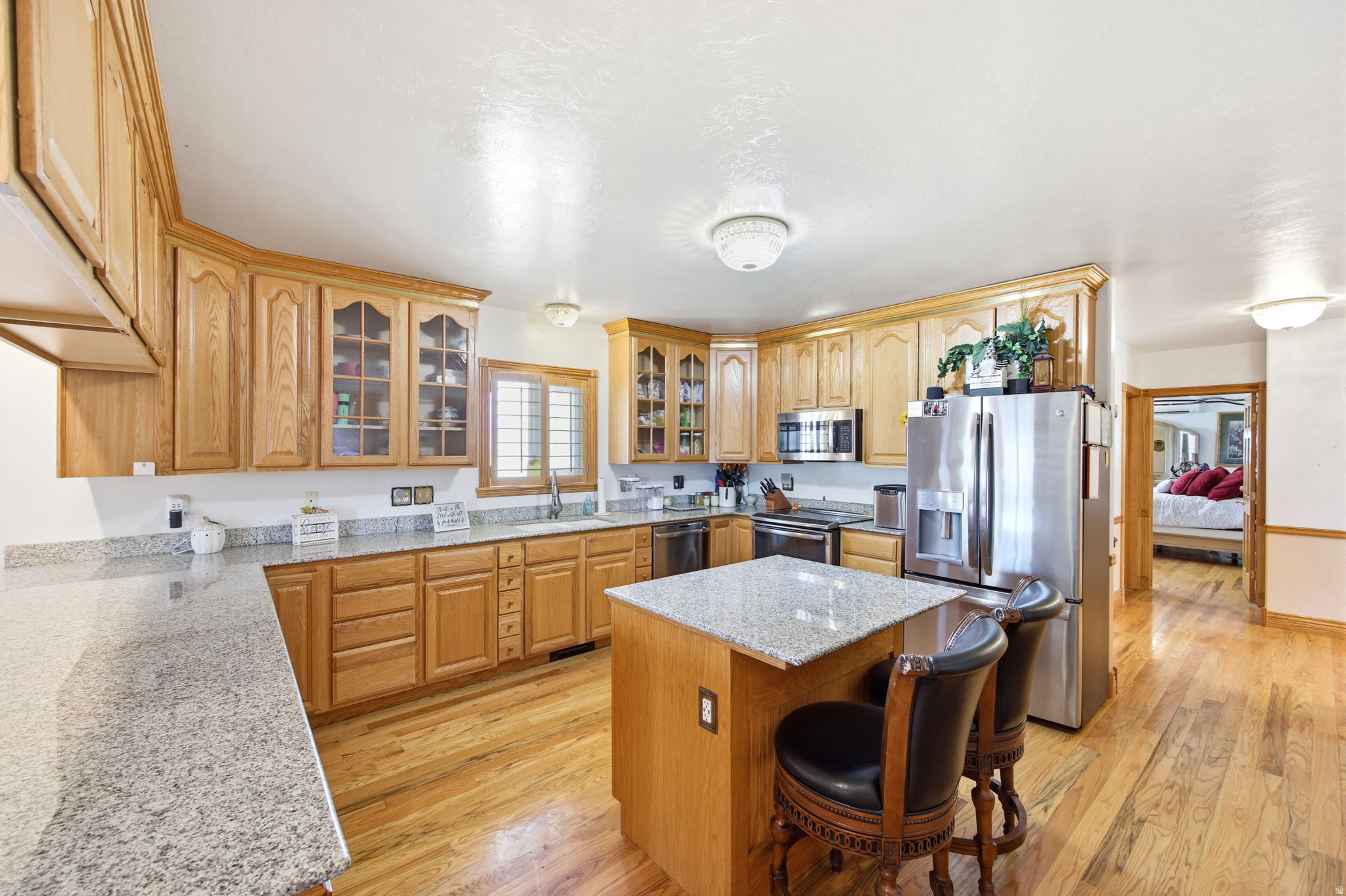 Main home - Kitchen featuring light wood cabinetry, stainless steel appliances, granite countertops, a kitchen island with seating, and wood-finish flooring