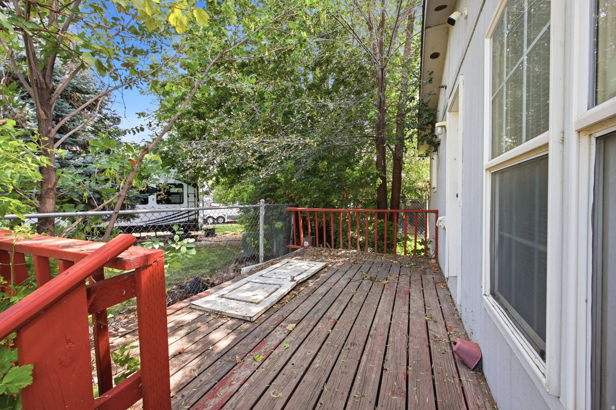 Wood-finish deck with red railing, bordered by a chain-link fence and mature trees