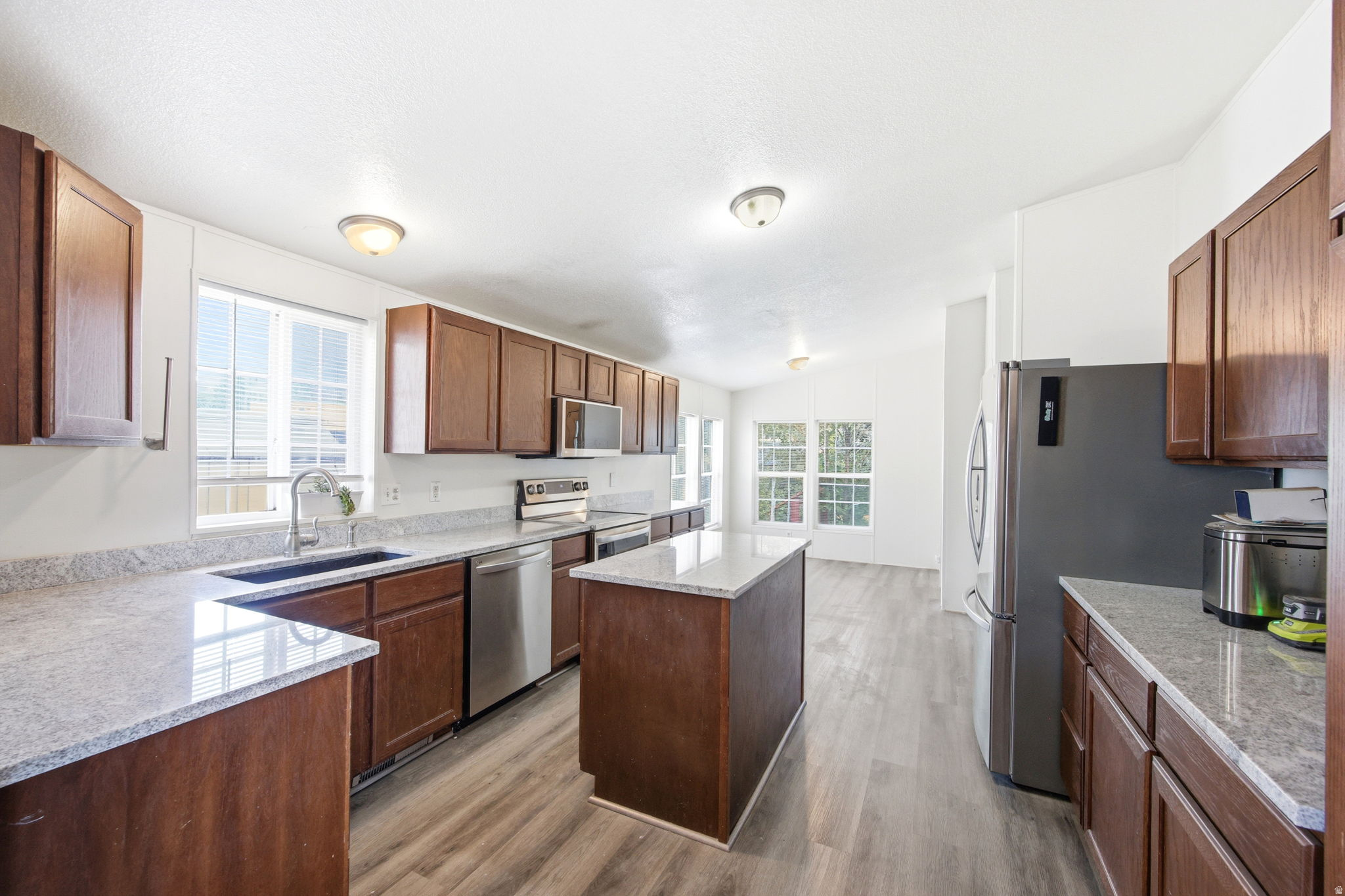 Modern kitchen featuring wood-finish flooring, ample cabinetry, granite-style countertops, stainless-steel appliances, and a central island