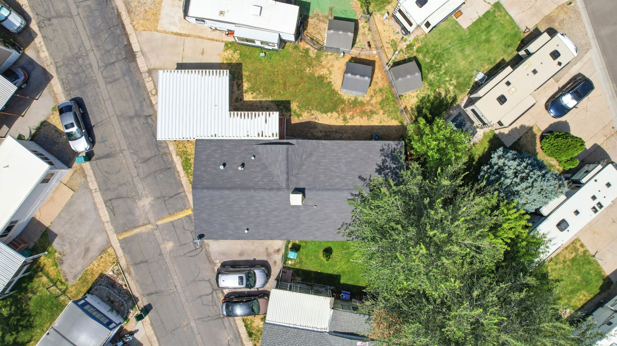 Aerial perspective showcasing a property with a dark shingle roof, established perimeter trees, and a paved street frontage