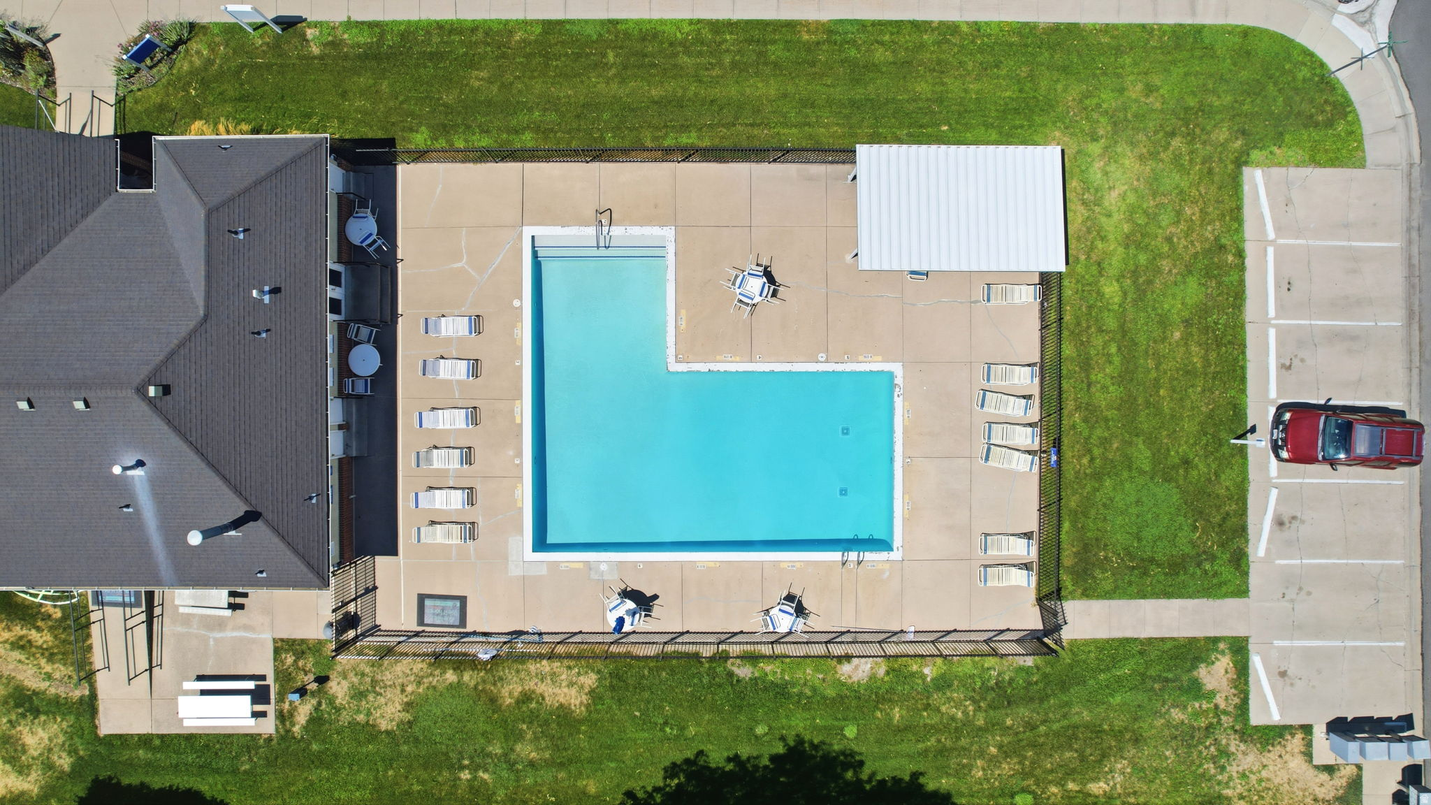 Aerial view showcasing a resort-style swimming pool with turquoise water and expansive sun deck featuring lounge seating, complemented by manicured lawn, detached garage with driveway parking, and contemporary home architecture with dark roofing and clean