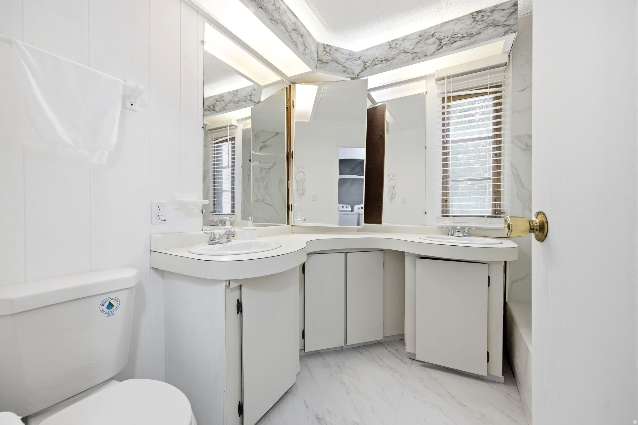 Bathroom featuring a dual vanity with integrated sinks, white cabinetry, and a full mirror wall