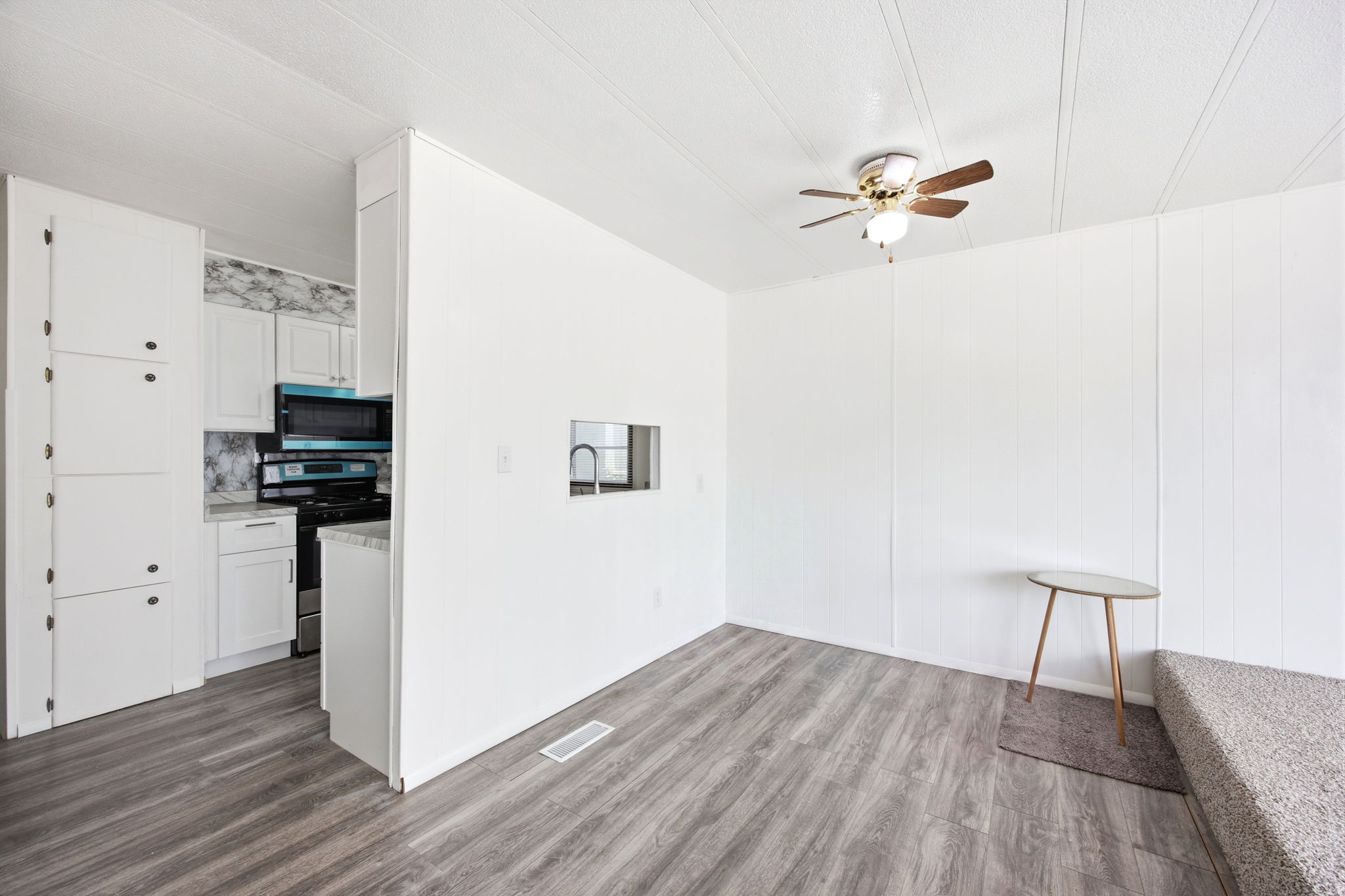 Open-concept living space featuring wood-finish flooring, a ceiling fan, and a pass-through window to the kitchen