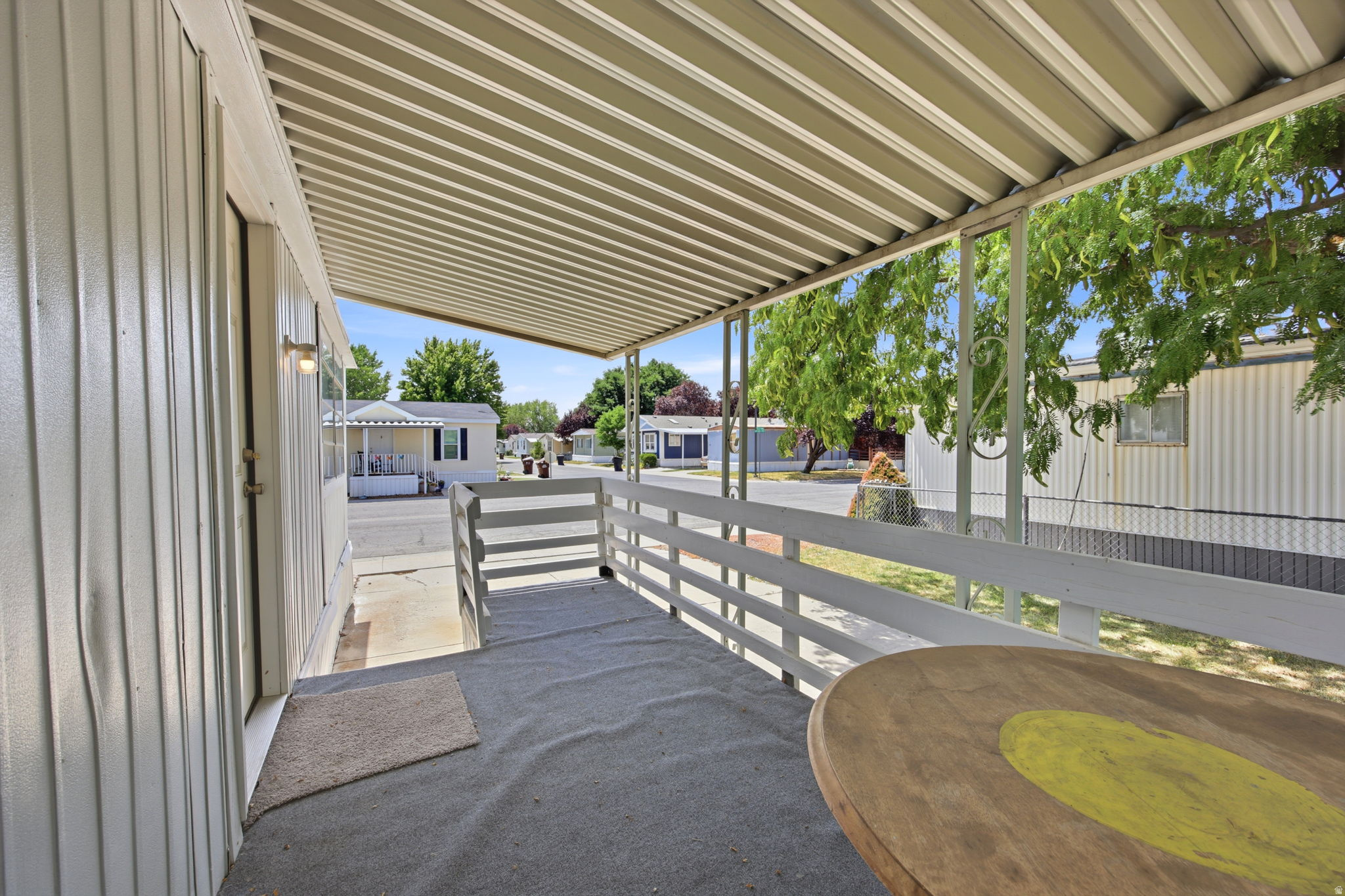 Covered patio with corrugated metal awning and horizontal white railings, featuring concrete flooring and shade from mature climbing vines
