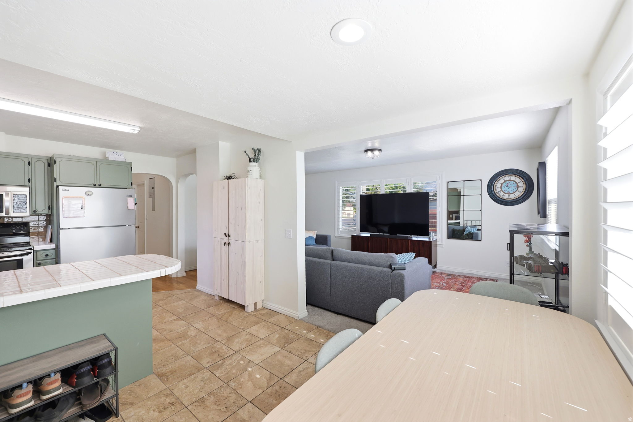 Open-concept living space featuring a kitchen with sage green cabinetry and a tiled breakfast bar, tile flooring, and white plantation shutters