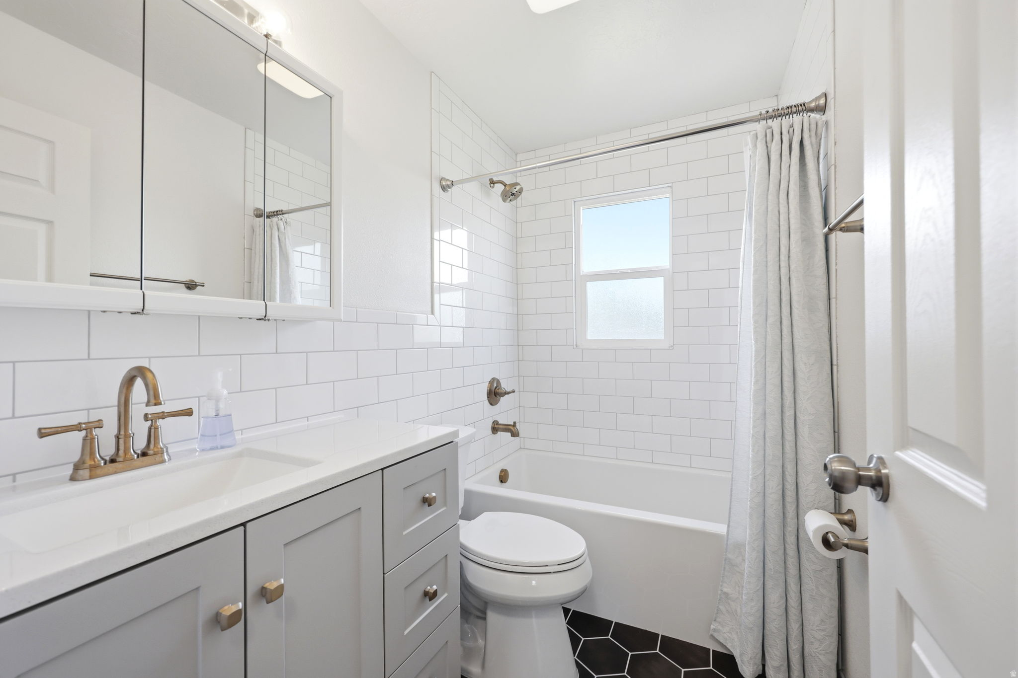 Bathroom featuring white subway tile walls, a light gray vanity with a white countertop, an integrated sink, and bronze-finish fixtures