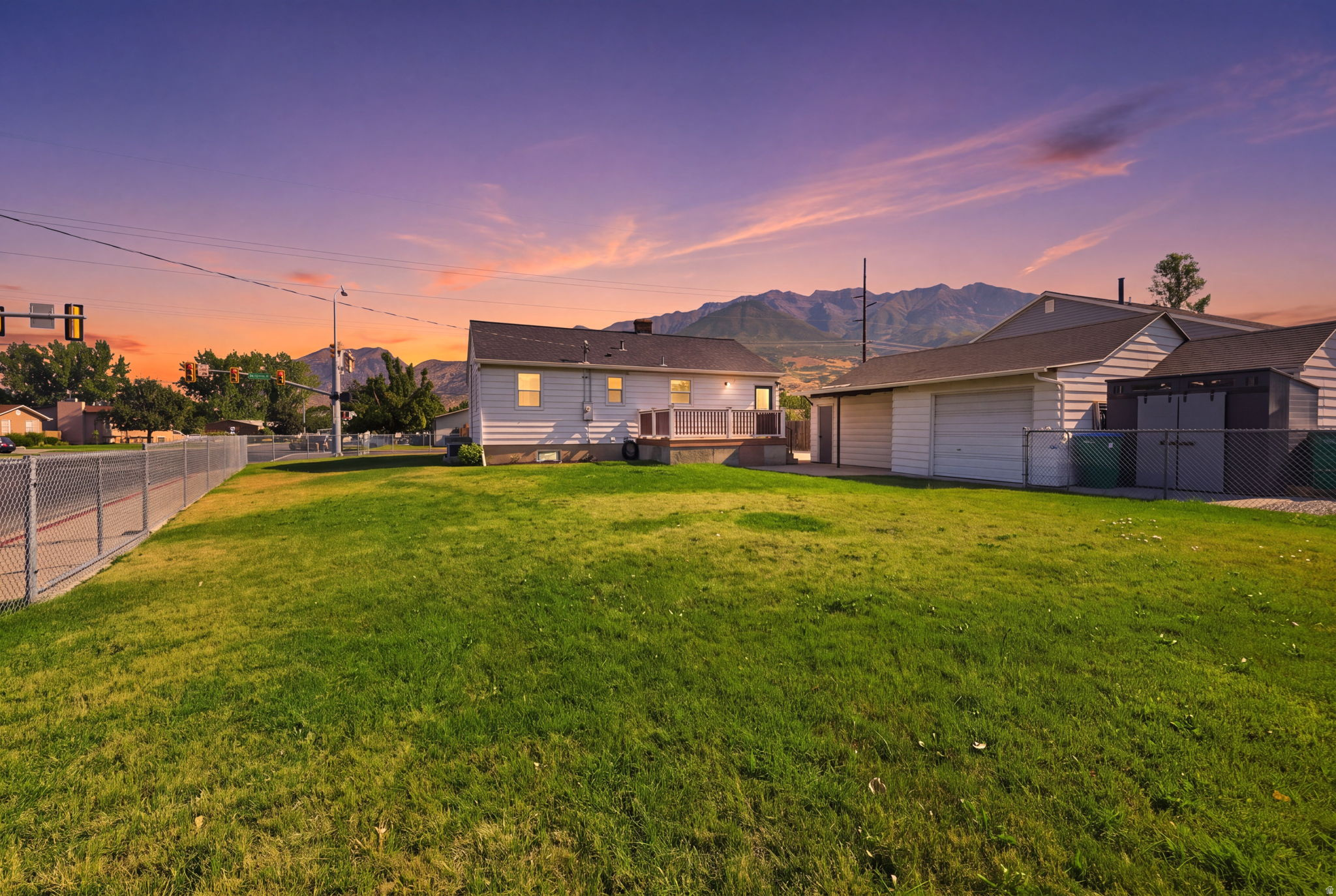 Expansive lawn area featuring a chain-link fence, a detached garage, and a rear deck