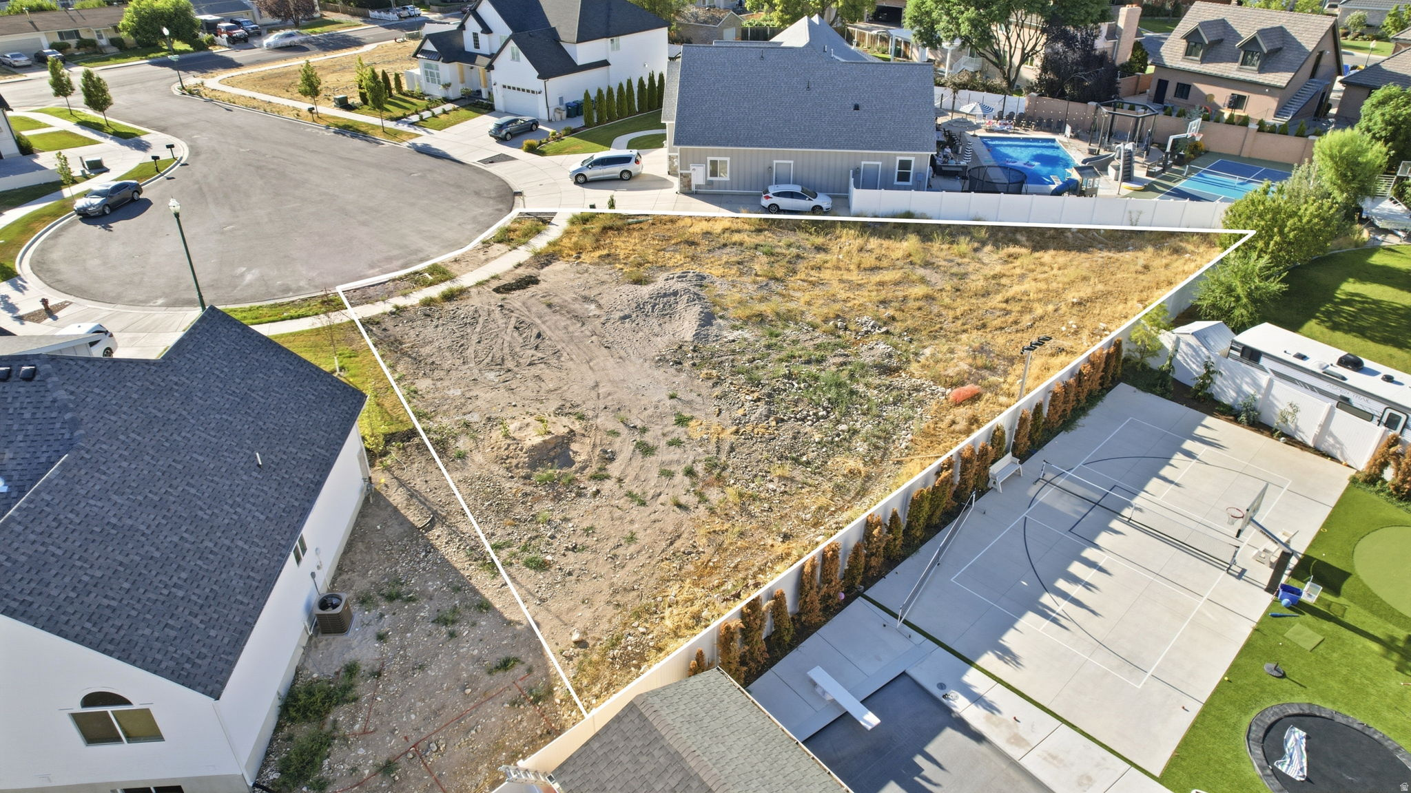 Cleared building lot with established curb and gutter, bordered by residential structures
