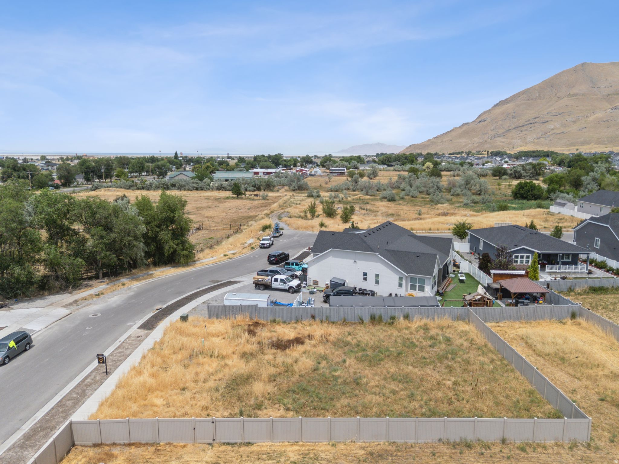 Expansive open lot featuring a perimeter fence, paved road frontage, and distant mountain scenery