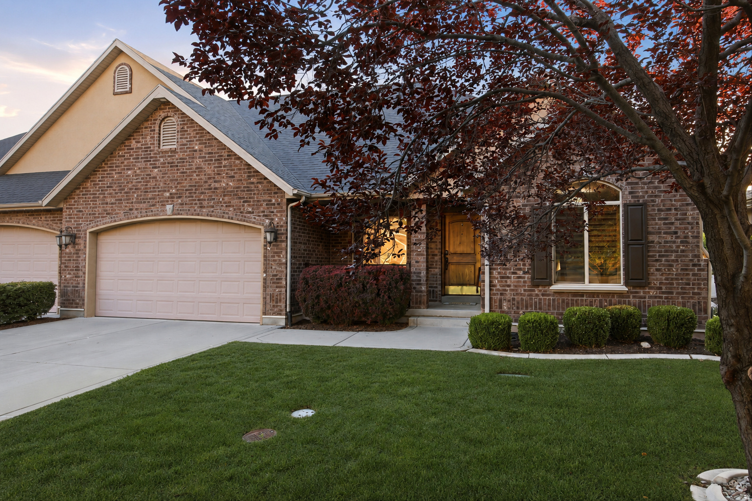 Brick facade residence featuring an attached two-car garage, manicured front lawn, and mature landscaping